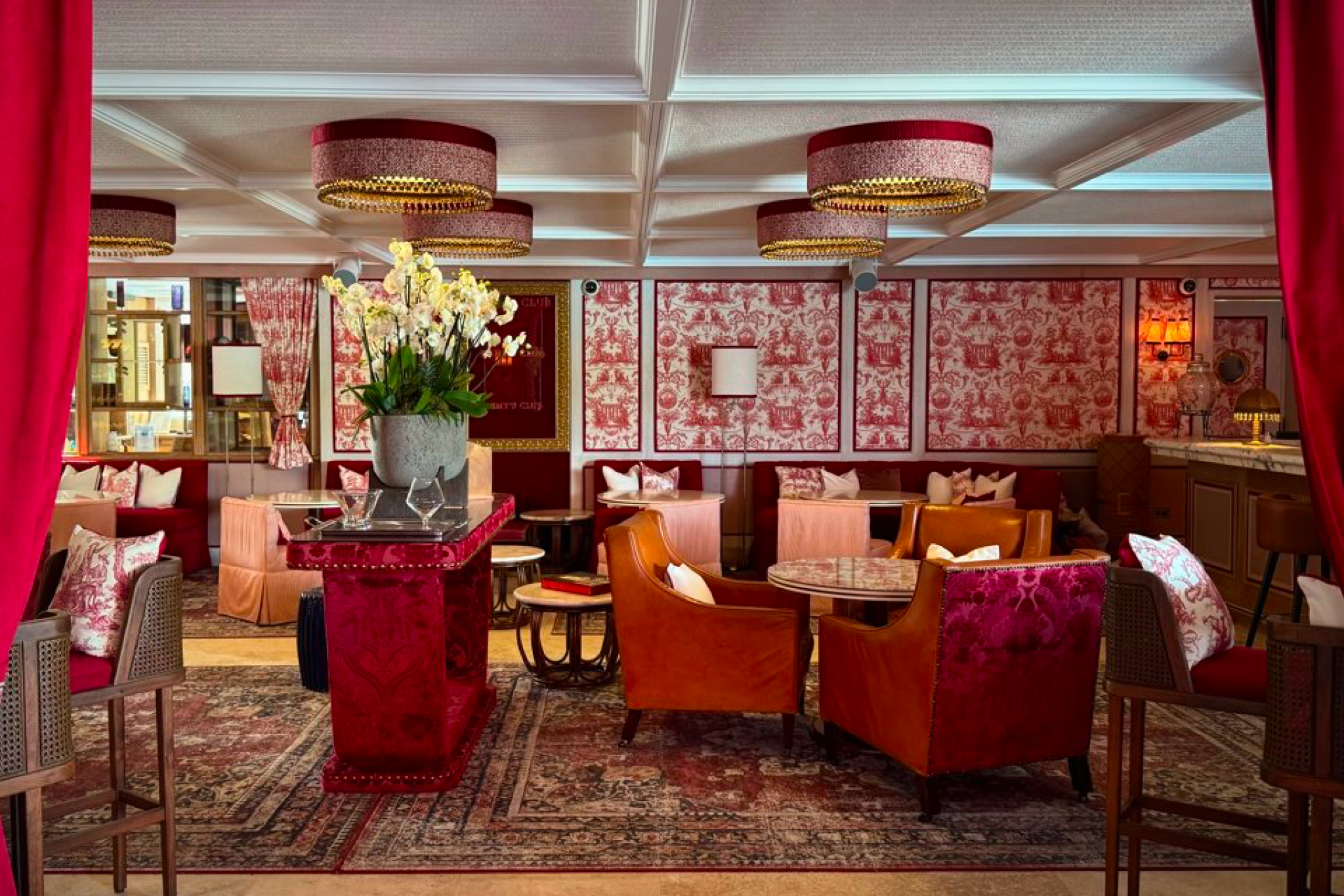 Interior of Rémy Bar & Salon at Eden Rock St. Barths, with red and gold accents, velvet chairs, and elegant lighting.