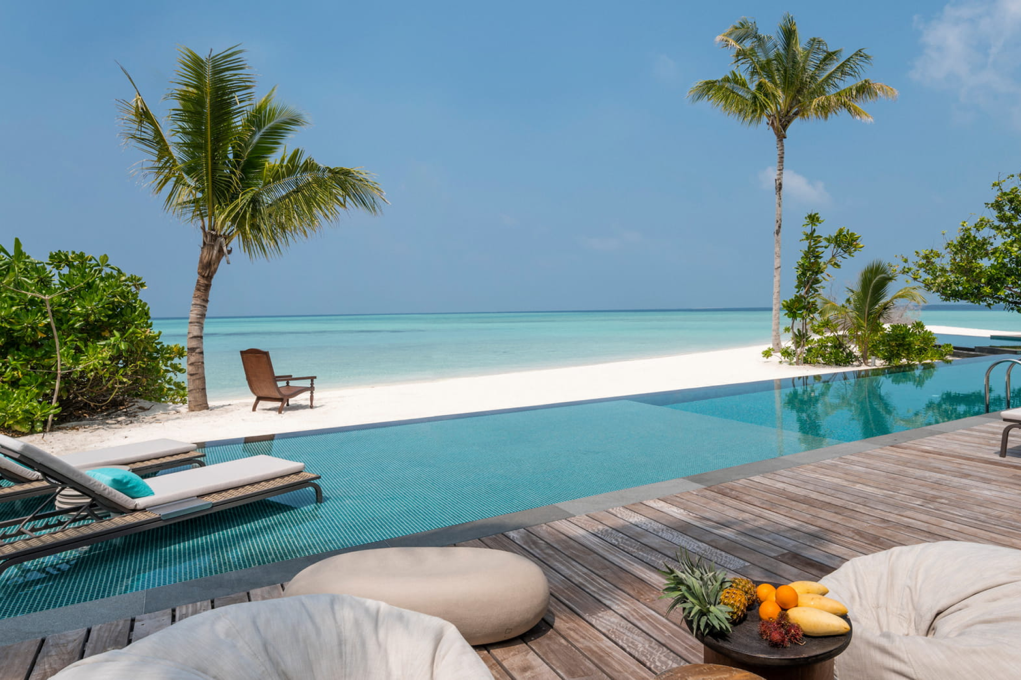 Infinity pool overlooking the ocean at Voavah, flanked by palm trees and surrounded by serene, white sand beach.