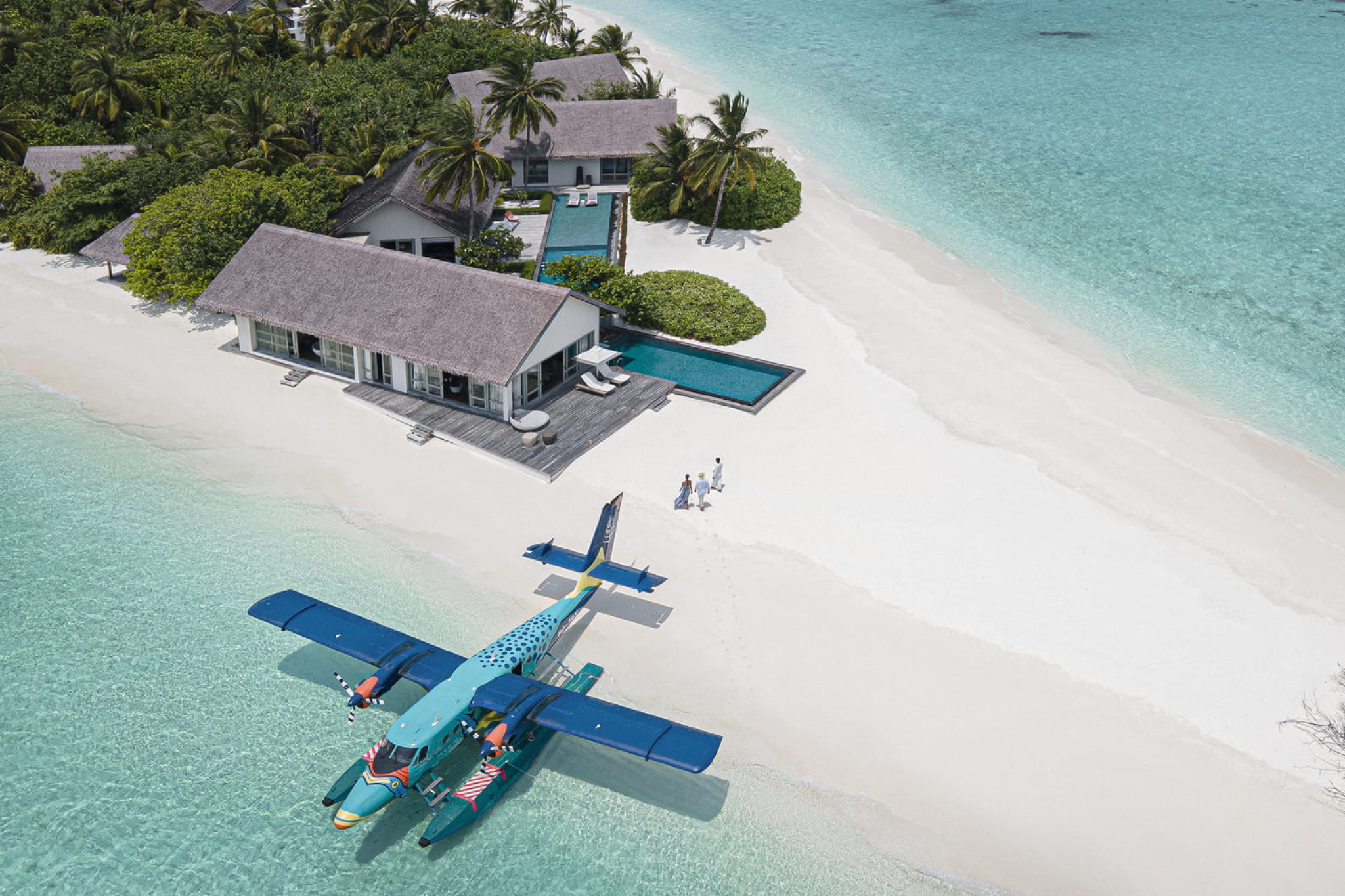 Colorful seaplane parked on the beach beside contemporary villas at Voavah, with guests walking along the white sand.