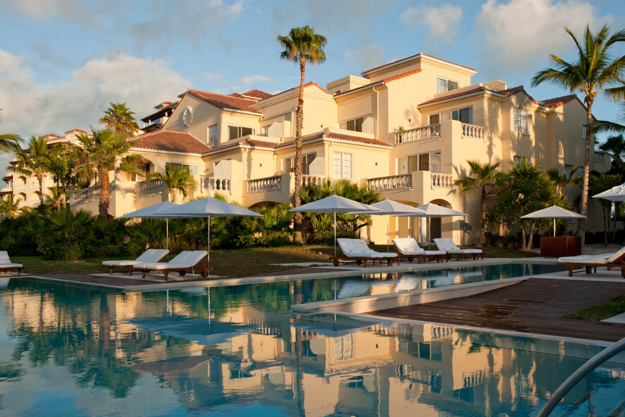 Grace Bay Club exterior with ocean-view suites and poolside loungers under palm trees.