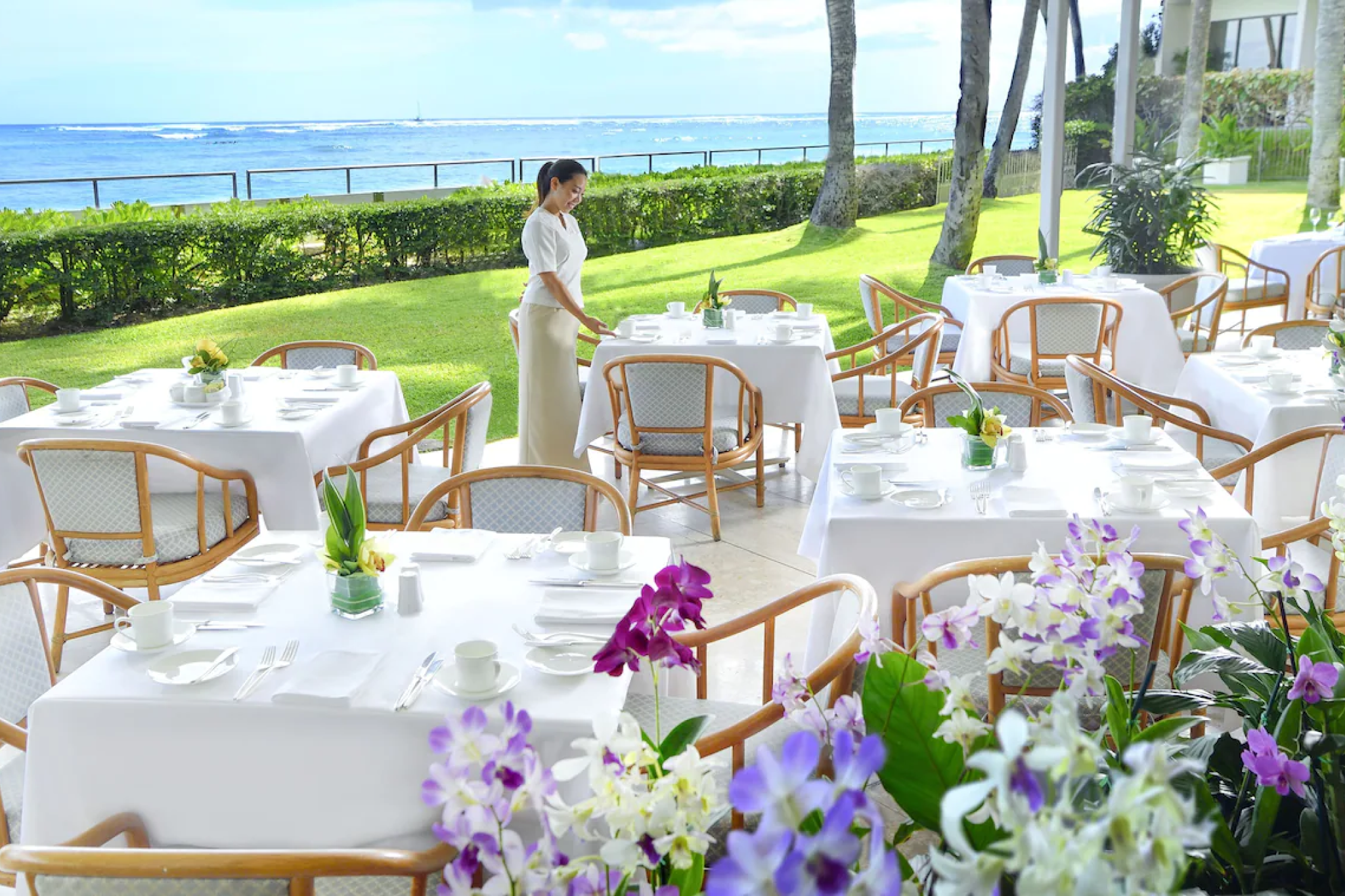 Seaside dining setup at Orchids restaurant at Halekulani Hotel, with ocean views, white linens, and lush tropical gardens.