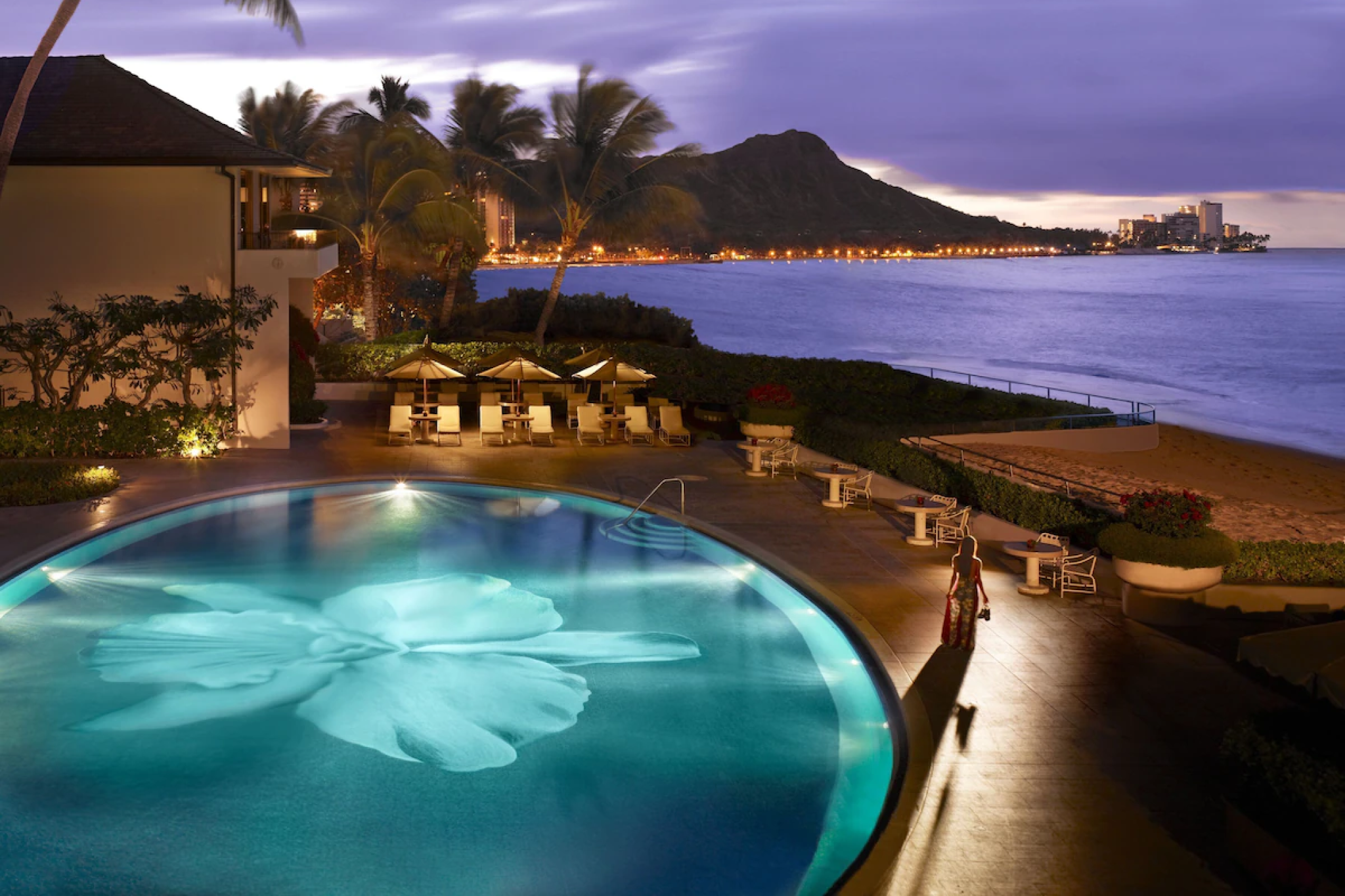 Halekulani Hotel’s iconic orchid mosaic pool at twilight, overlooking Diamond Head and the calm waters of Waikiki Beach.