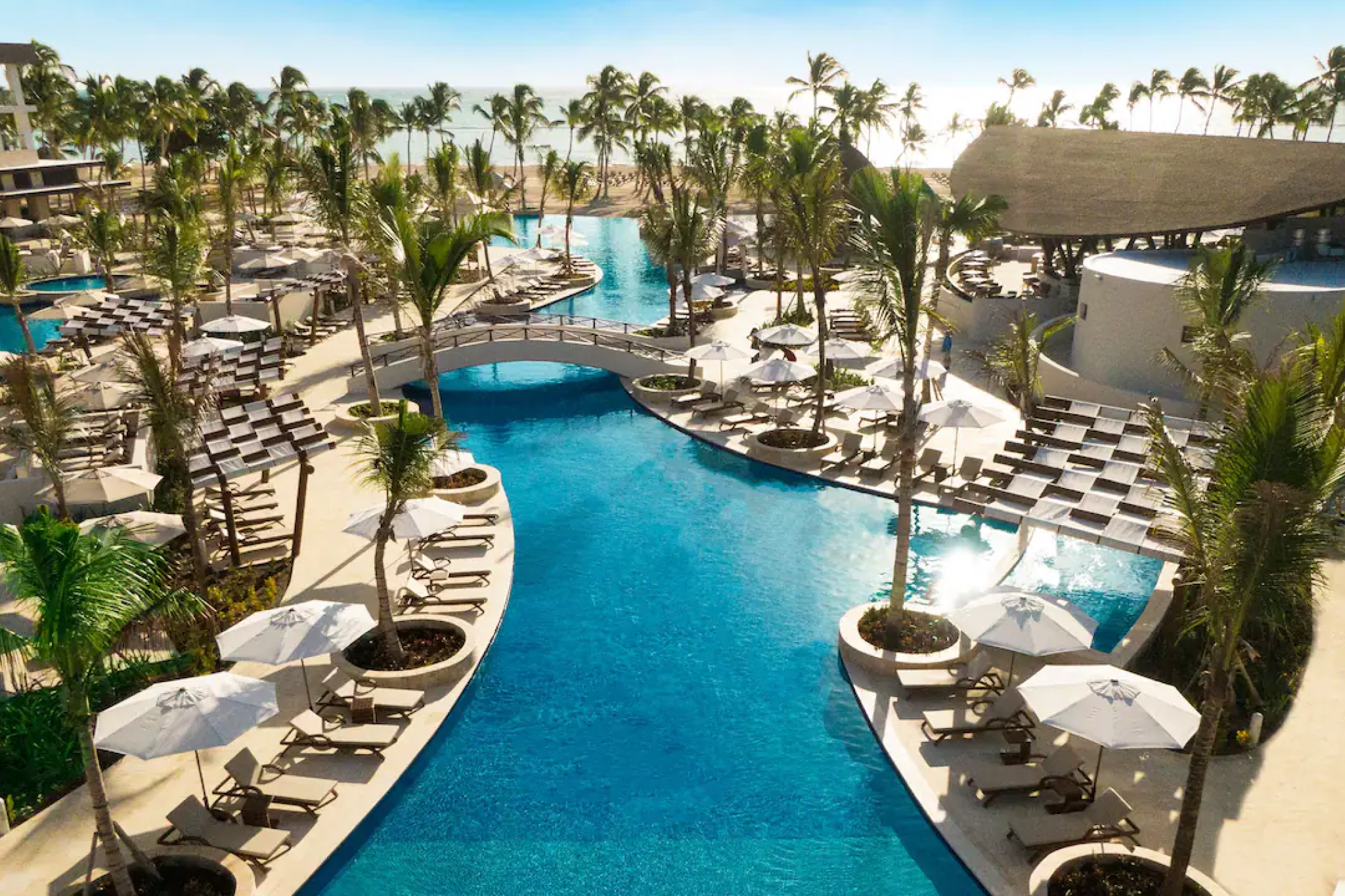 Expansive swimming pool surrounded by palm trees and lounge chairs at Hyatt Ziva Cap Cana.