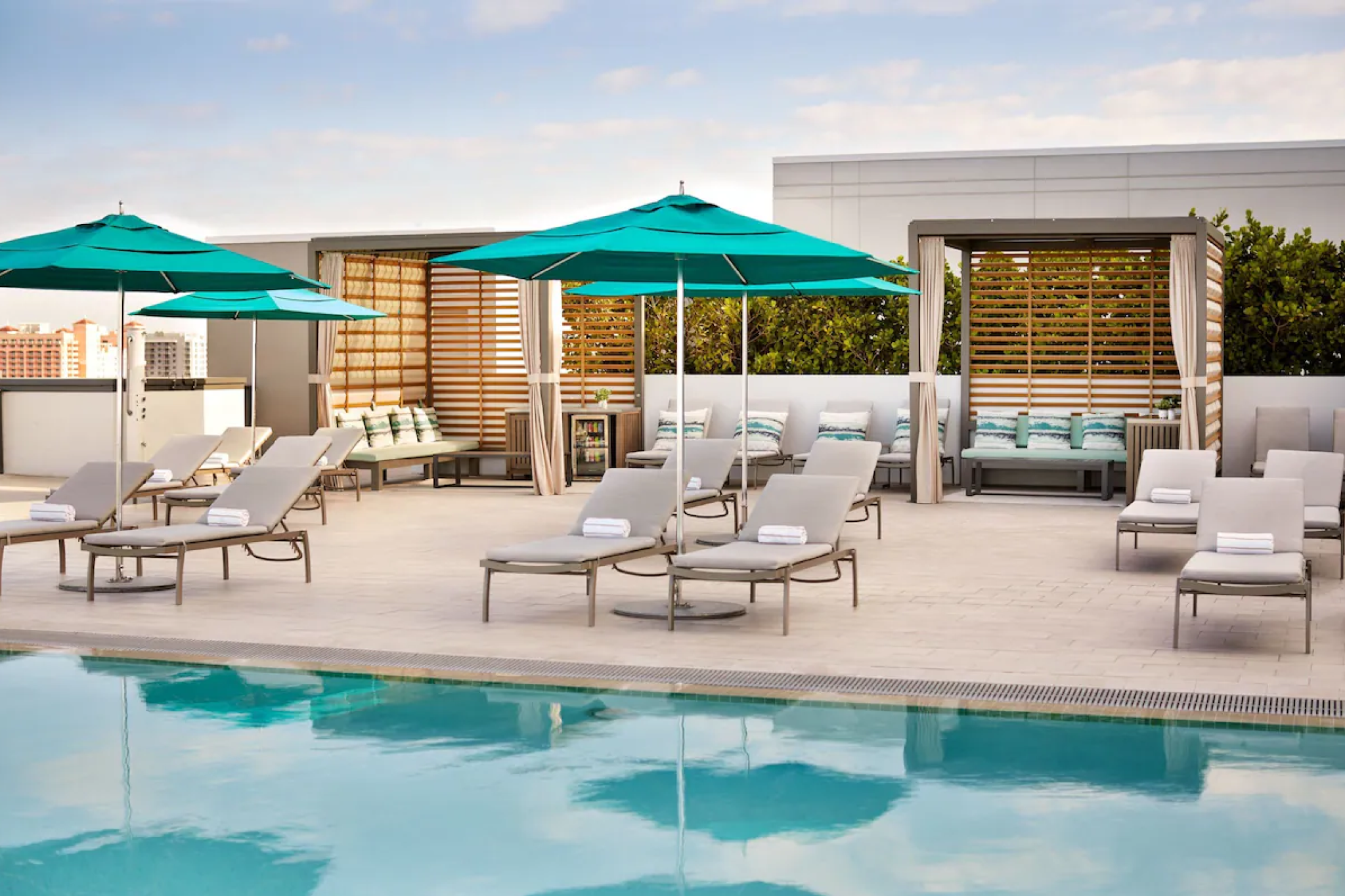Rooftop pool at JW Marriott Clearwater Beach Resort & Spa with sleek sun loungers, teal umbrellas, and upscale cabanas designed for elevated relaxation against a backdrop of clear skies and lush greenery.