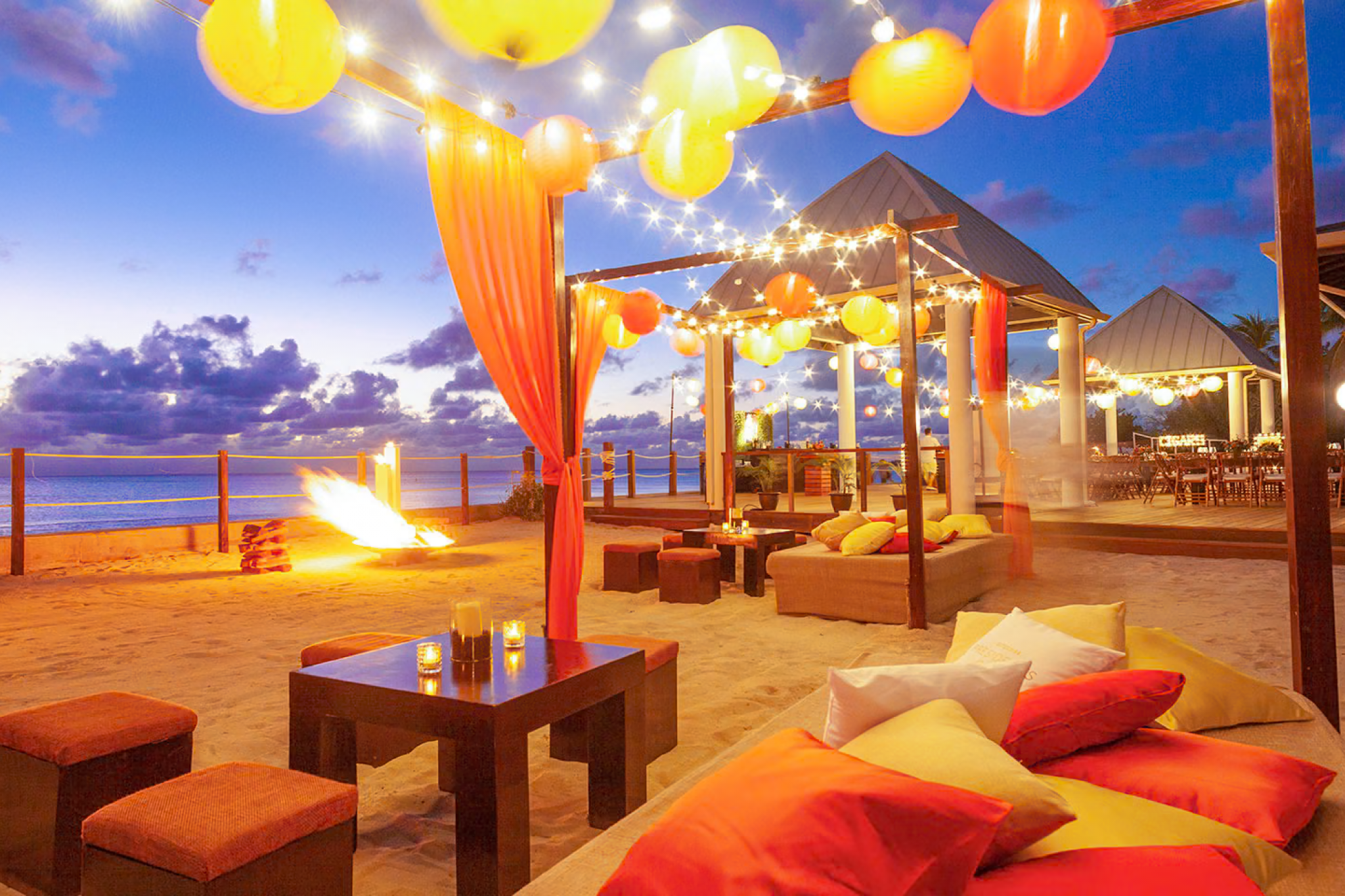 Panoramic view of Kimpton Seafire Resort + Spa at sunset, with illuminated pools and the Caribbean Sea beyond.