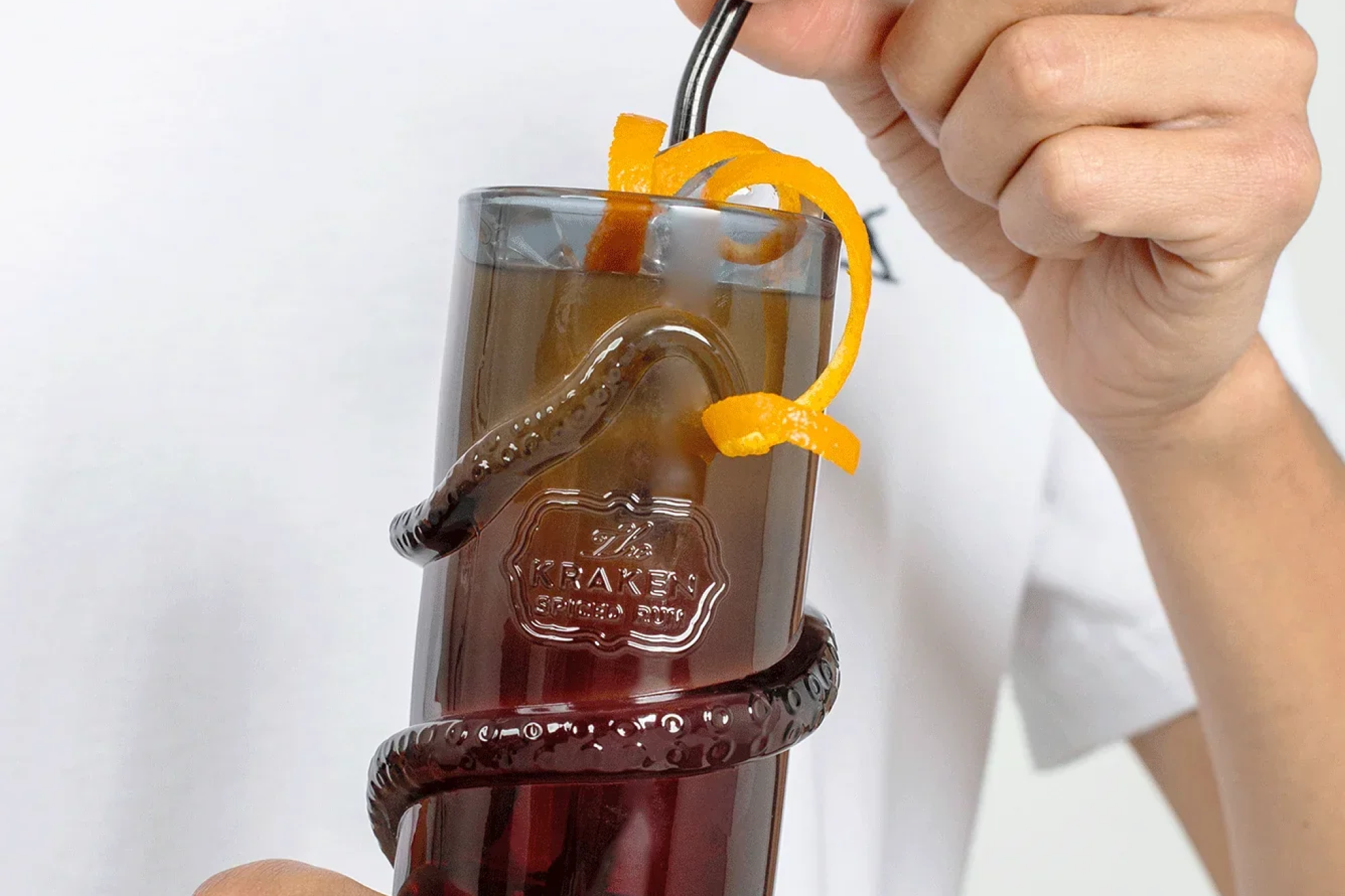 Kraken Black Spiced Rum bottle beside a cocktail glass wrapped in a tentacle-shaped base, garnished with orange peel and a straw.