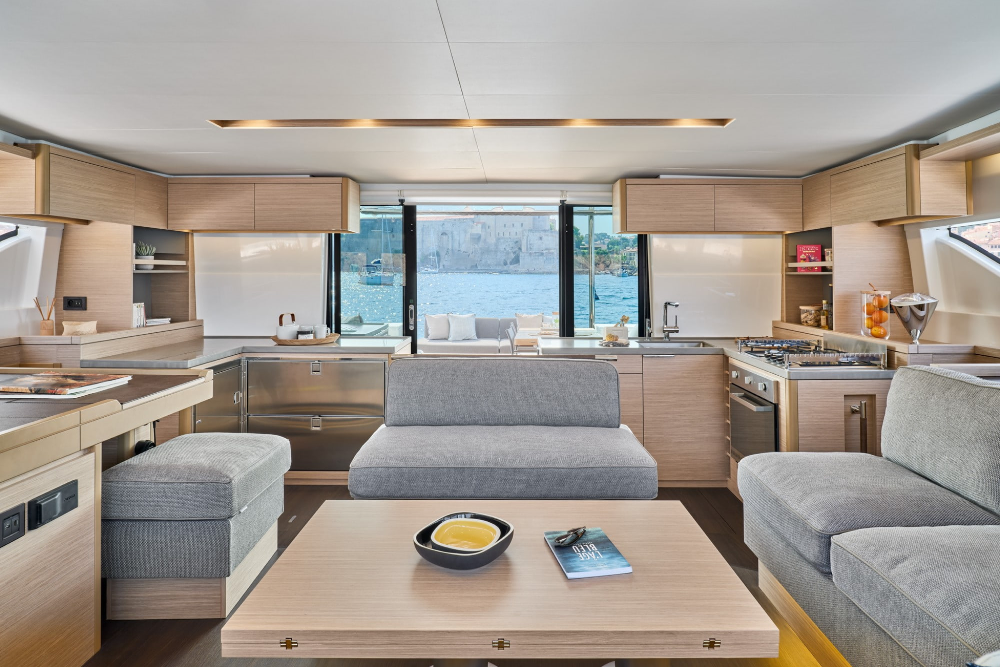 Interior view of the Lagoon 51 catamaran’s saloon, featuring light wood finishes, an open galley, and panoramic views over the water.