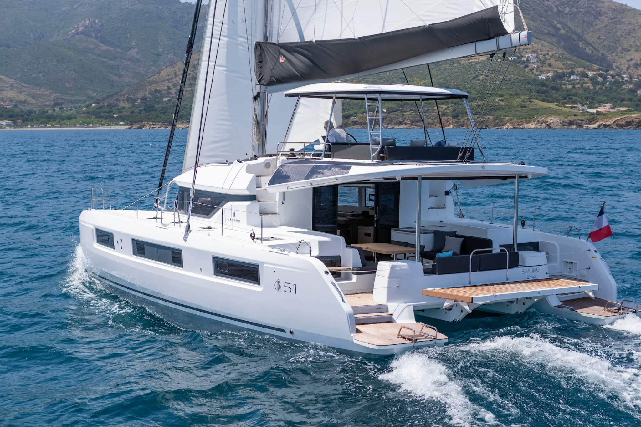 Lagoon 51 catamaran under sail, highlighting its dual-hull design, flybridge helm station, and well-appointed aft cockpit.