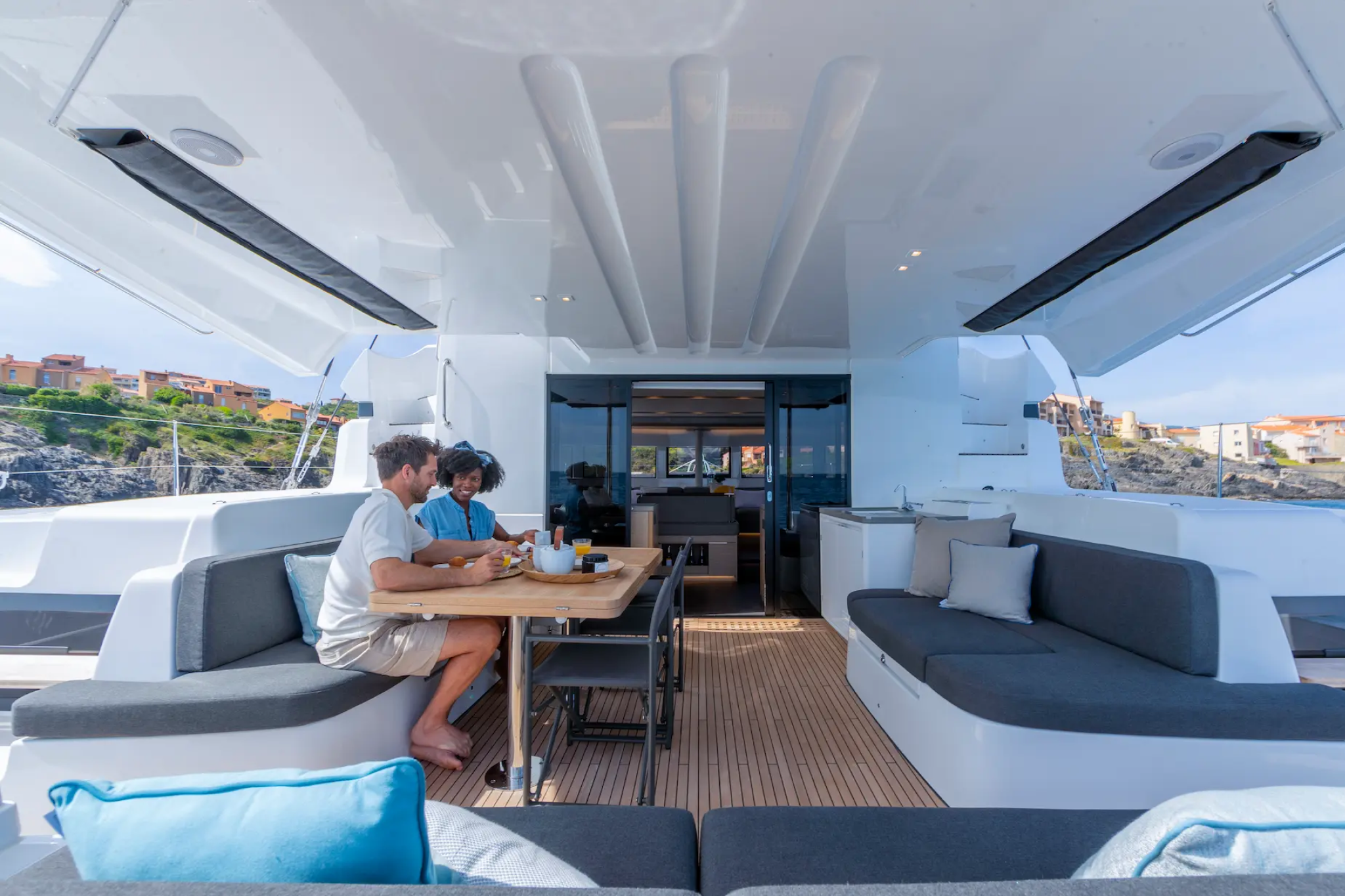 Couple relaxing on the forward sun lounge of the Lagoon 51 catamaran, with a view of the trampoline and sleek deck layout under sail.