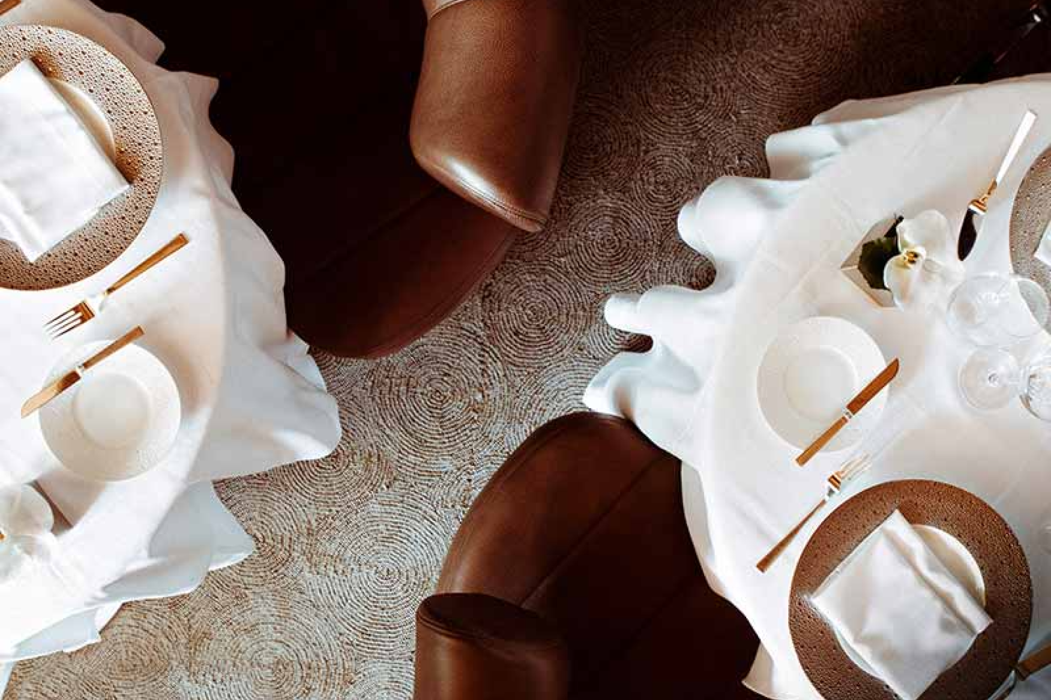 Overhead view of two elegantly set tables with leather chairs at Le Bernardin’s dining room in New York City.