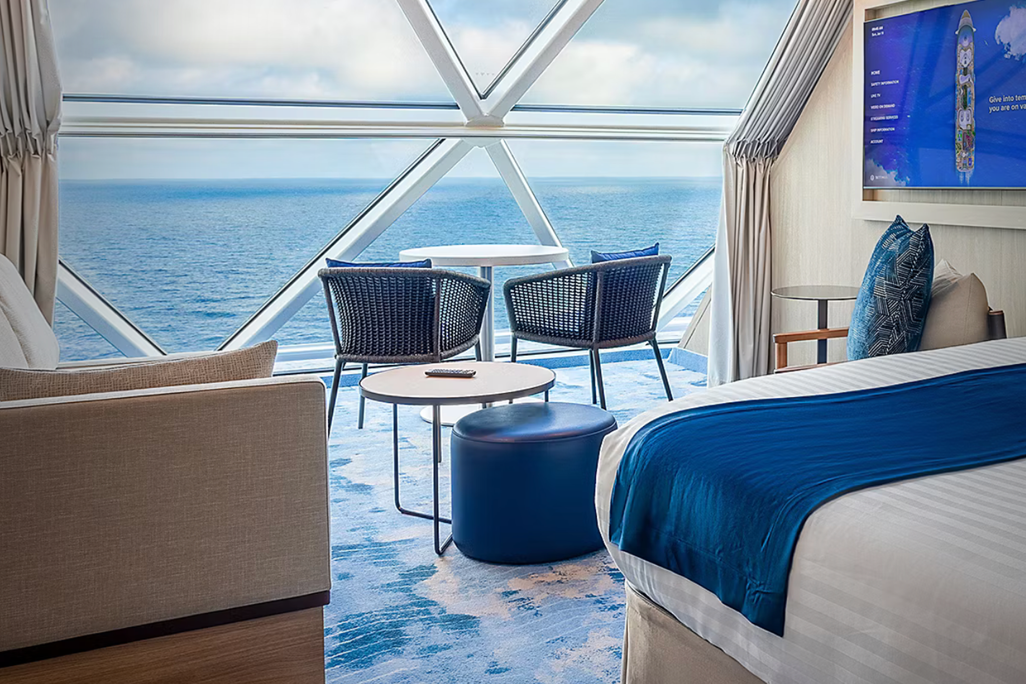 Interior of a premium stateroom aboard Legend of the Seas featuring floor-to-ceiling windows, a private seating area, and sweeping ocean views