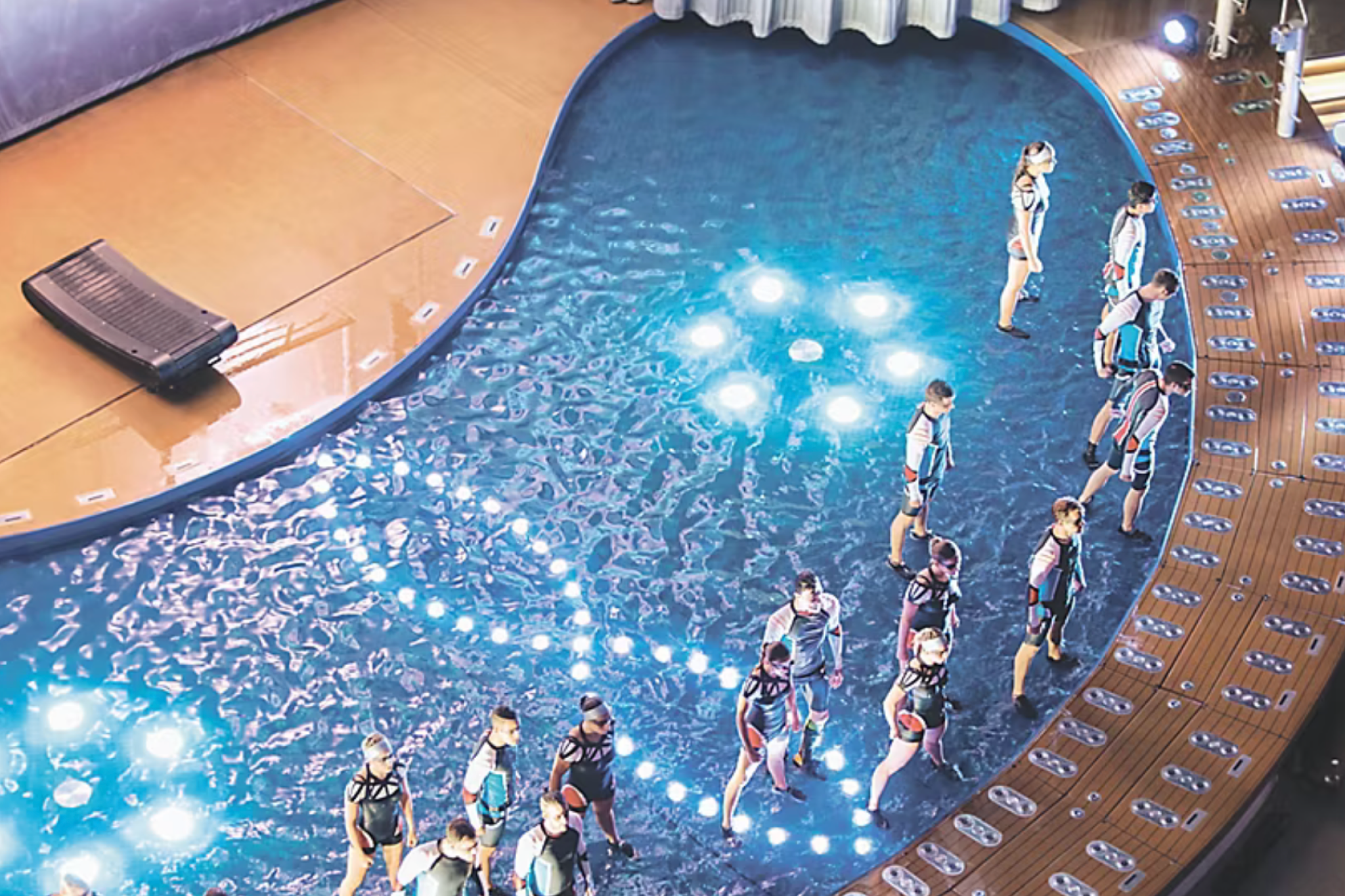 Evening aqua show on Legend of the Seas with performers in wetsuits standing in a glowing circular pool surrounded by theater seating