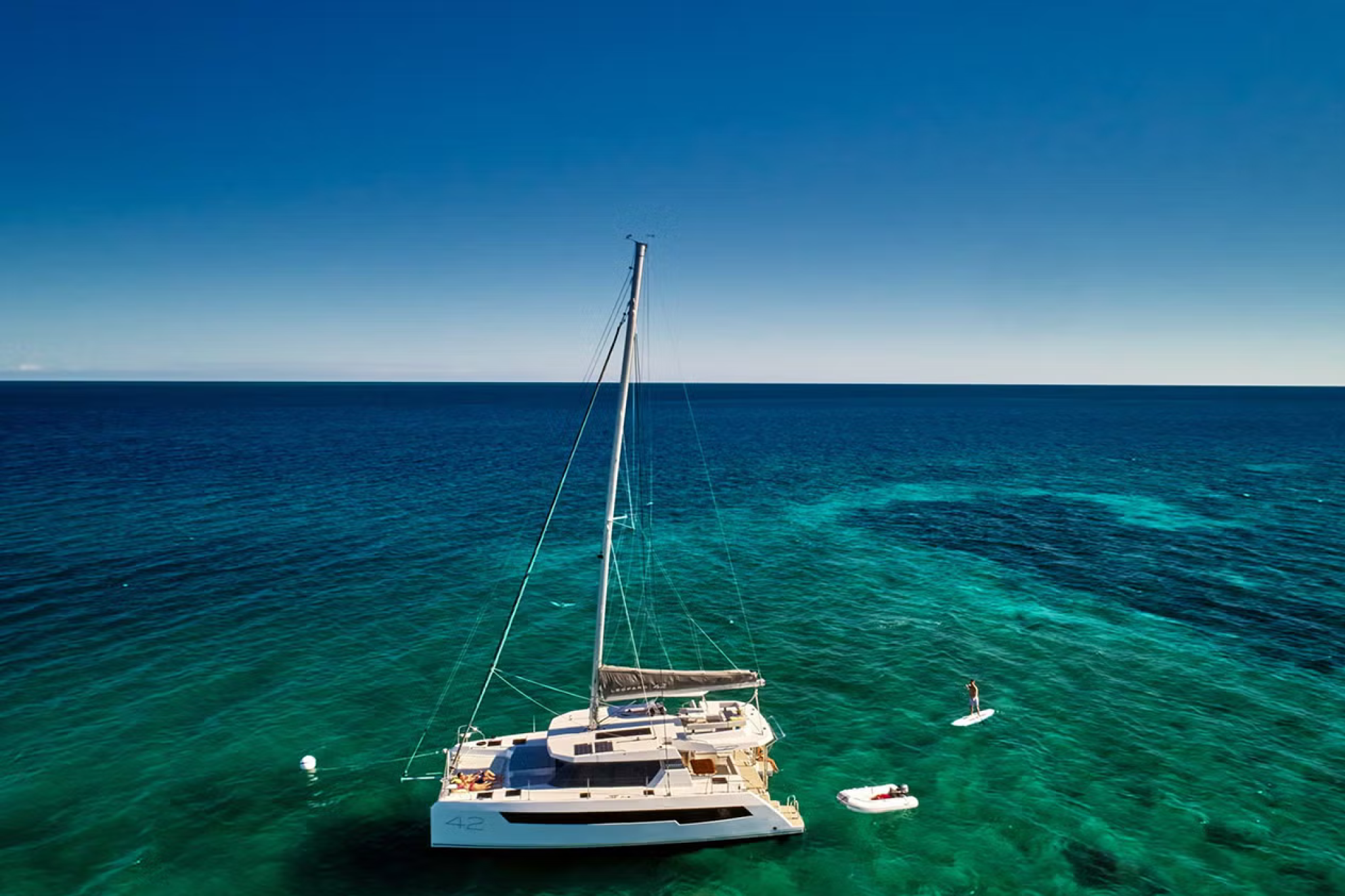 Aerial view of the Leopard 42 catamaran anchored in clear turquoise waters, with paddleboards and a tender nearby.
