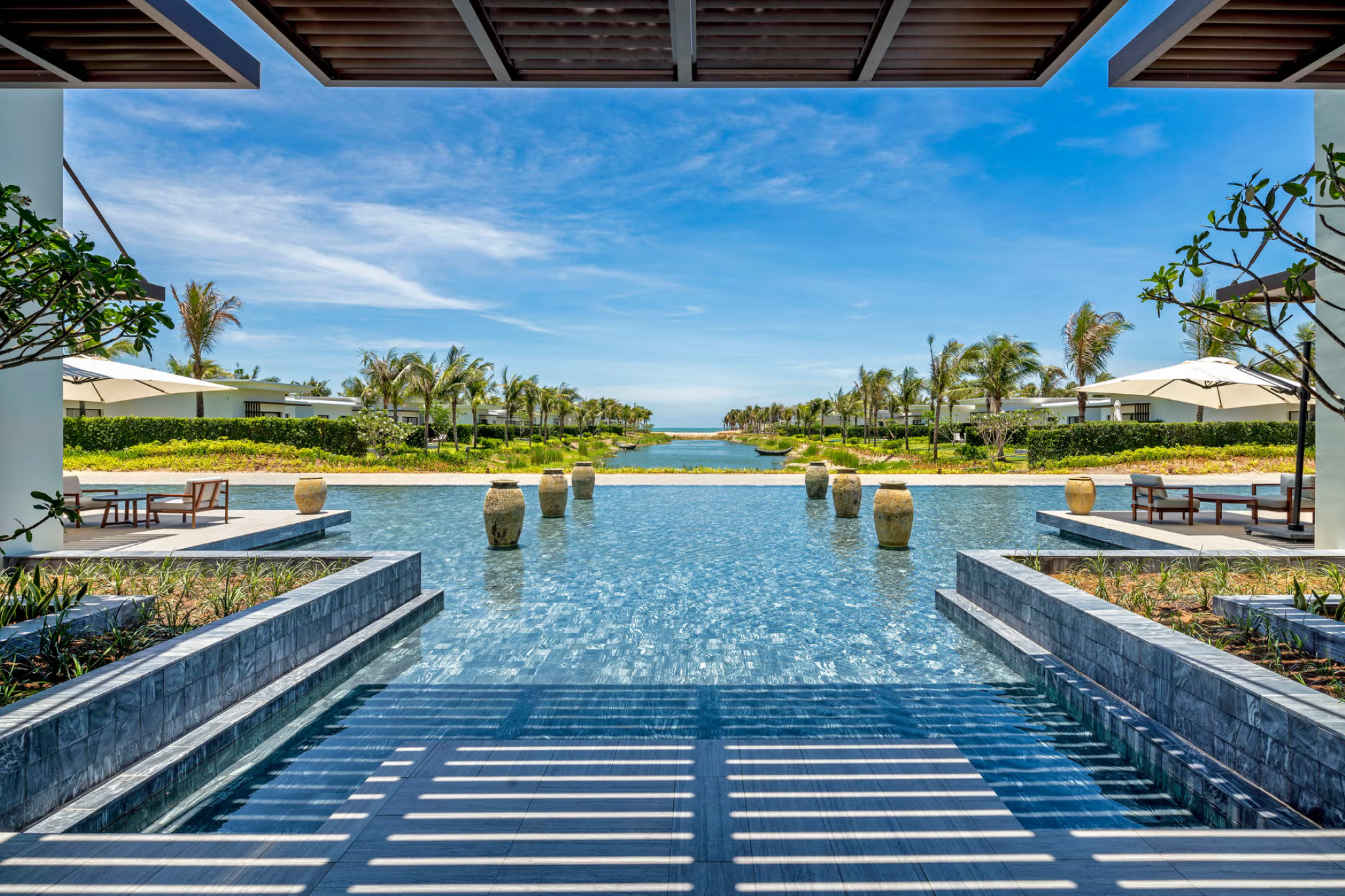Infinity pool at Melia Ho Tram Beach Resort overlooking the ocean, surrounded by sun loungers and palm trees.