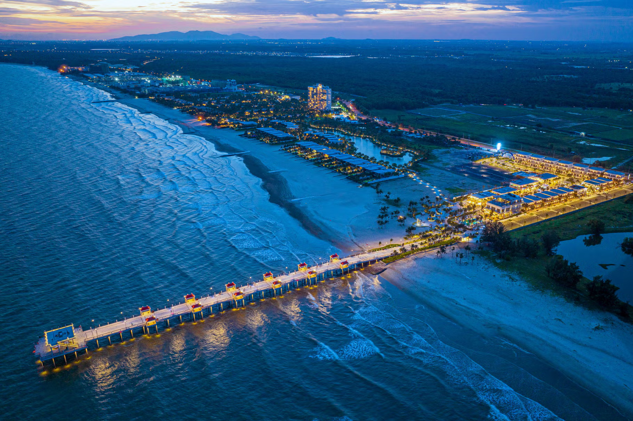 Panoramic view of Melia Ho Tram Beach Resort at sunset, with illuminated pools and beachfront villas.