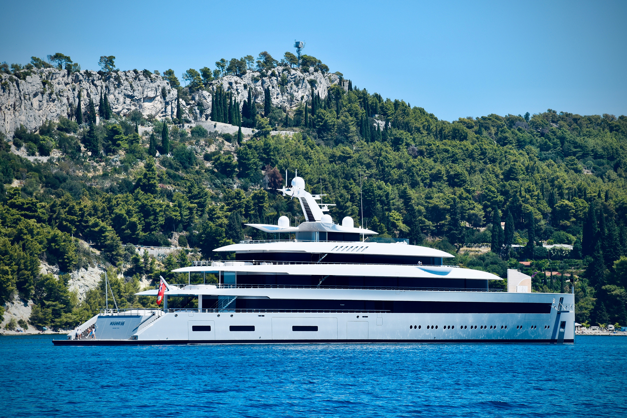 A luxurious superyacht gliding through calm waters with a rocky coastline in the background, illustrating one of the Most Fascinating Superyacht Facts about modern yacht design and engineering.