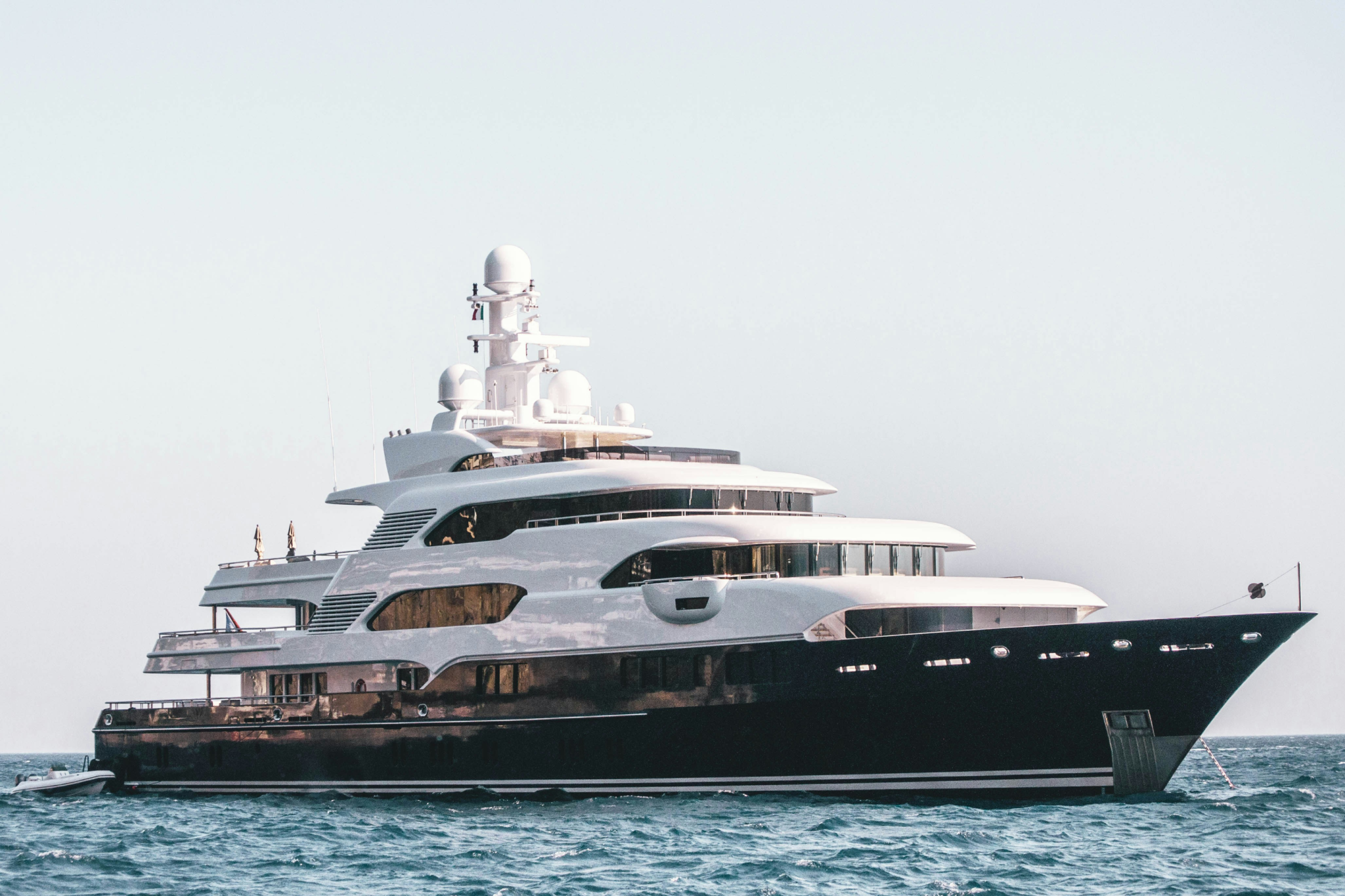 A multi-deck superyacht docked near a scenic coastline, showcasing the scale and luxury that highlight the Most Fascinating Superyacht Facts about space and amenities on board.