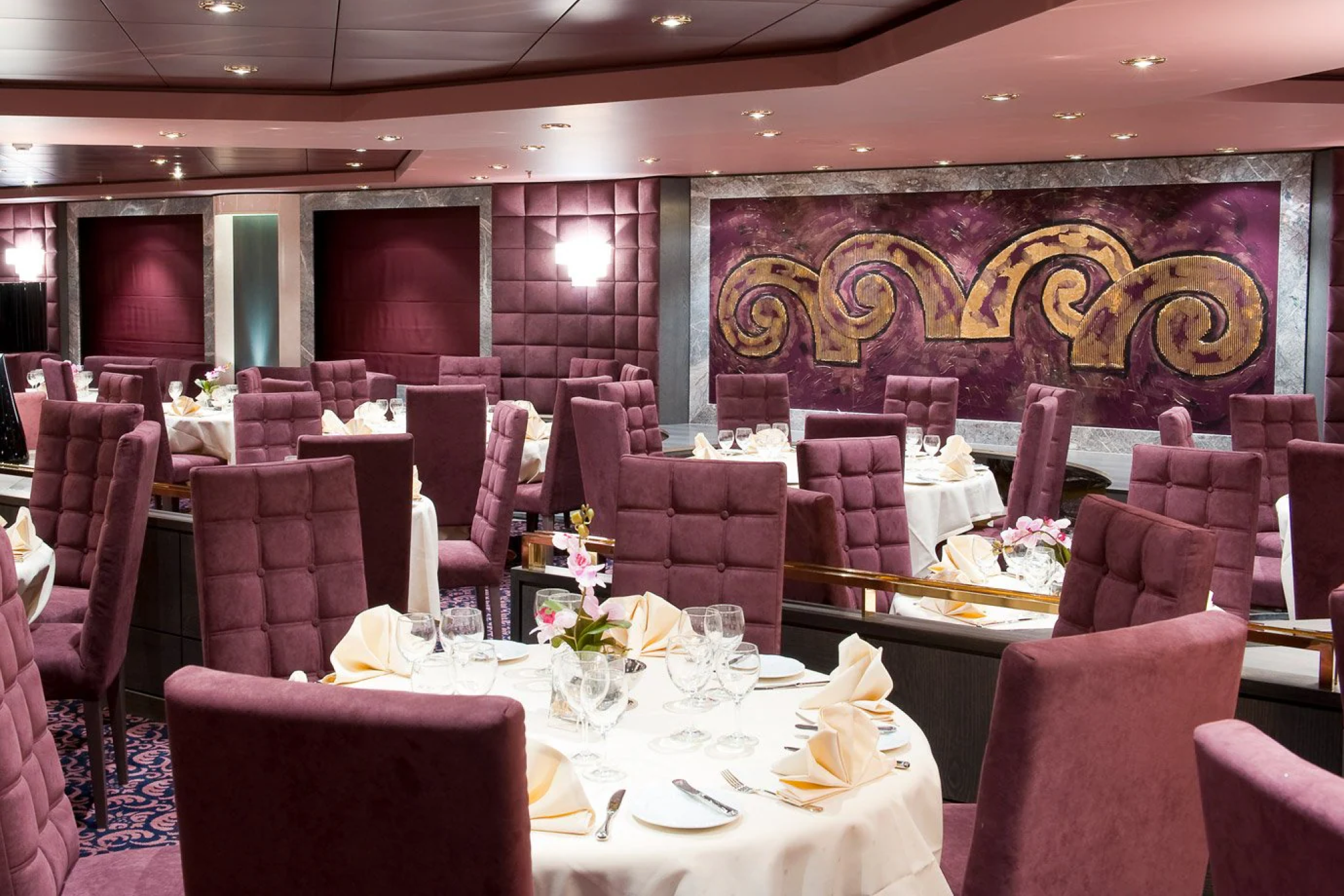 Elegant main dining room on MSC Magnifica with plush purple seating, white tablecloths, and gold-accented wall art.