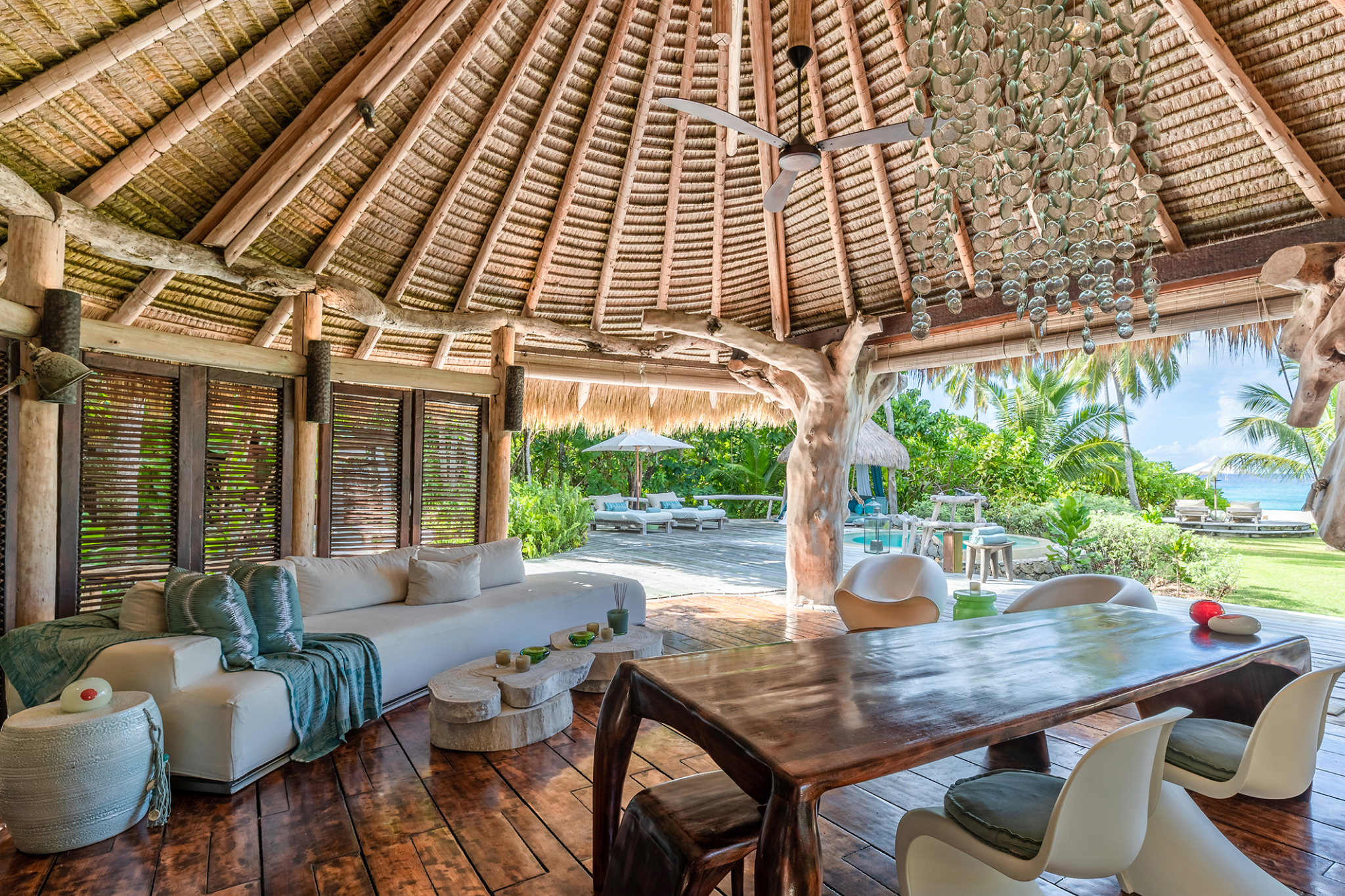 Open-air villa lounge at North Island Seychelles with thatched roof, driftwood furniture, and views of tropical gardens leading to the ocean. north_island_seychelles_villas.png
