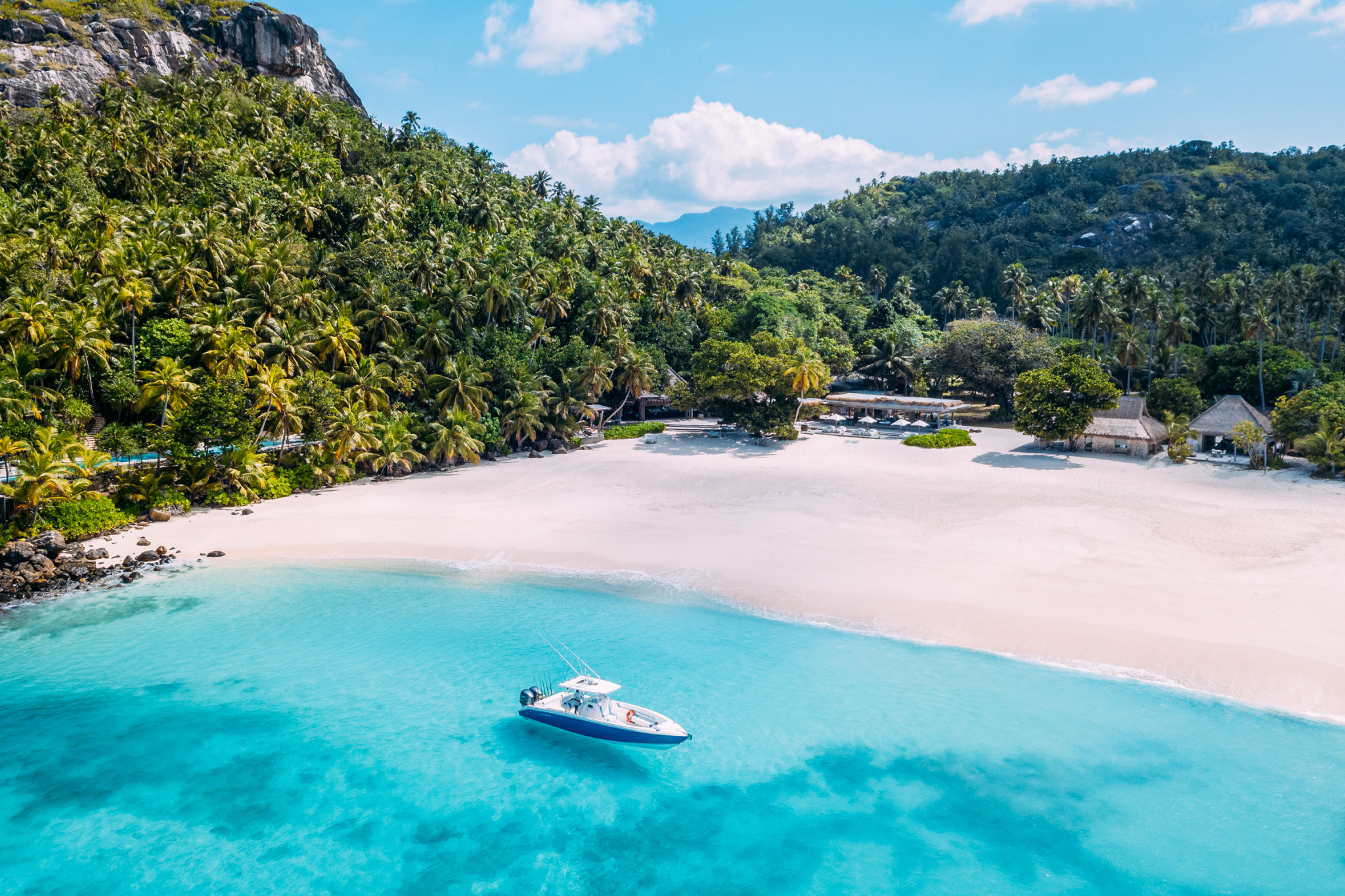A luxury yacht anchored off a white-sand beach at North Island Seychelles, showcasing the pristine turquoise waters and lush tropical jungle backdrop.
