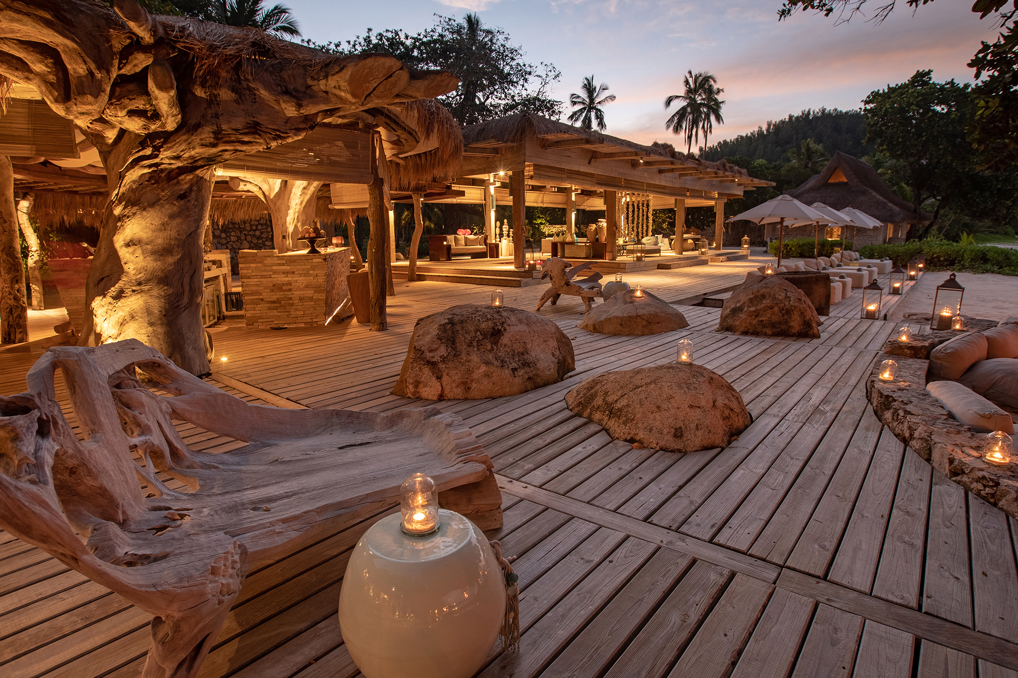 Evening dining area at North Island Seychelles with lanterns, driftwood seating, and natural stone accents creating a rustic luxury atmosphere.
