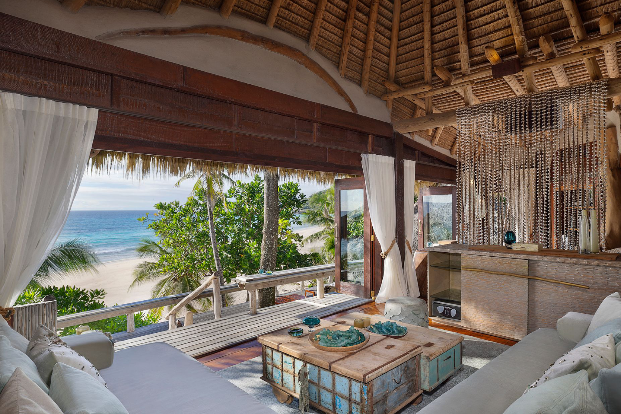 Villa interior at North Island Seychelles with natural wood design, ocean-facing balcony, and uninterrupted views of the beach and turquoise water.