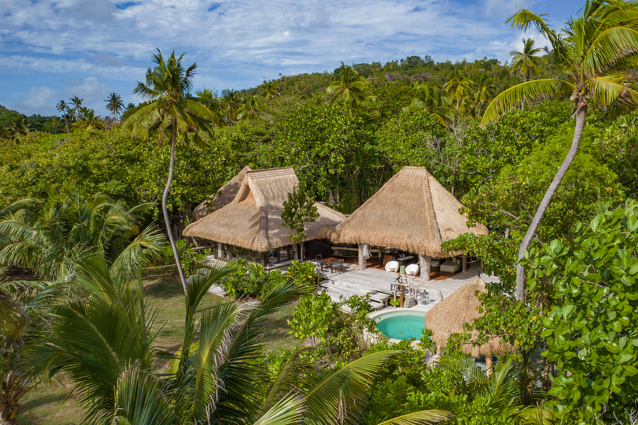 Private villa at North Island Seychelles nestled among dense greenery, featuring thatched roofs, a plunge pool, and expansive outdoor living space.