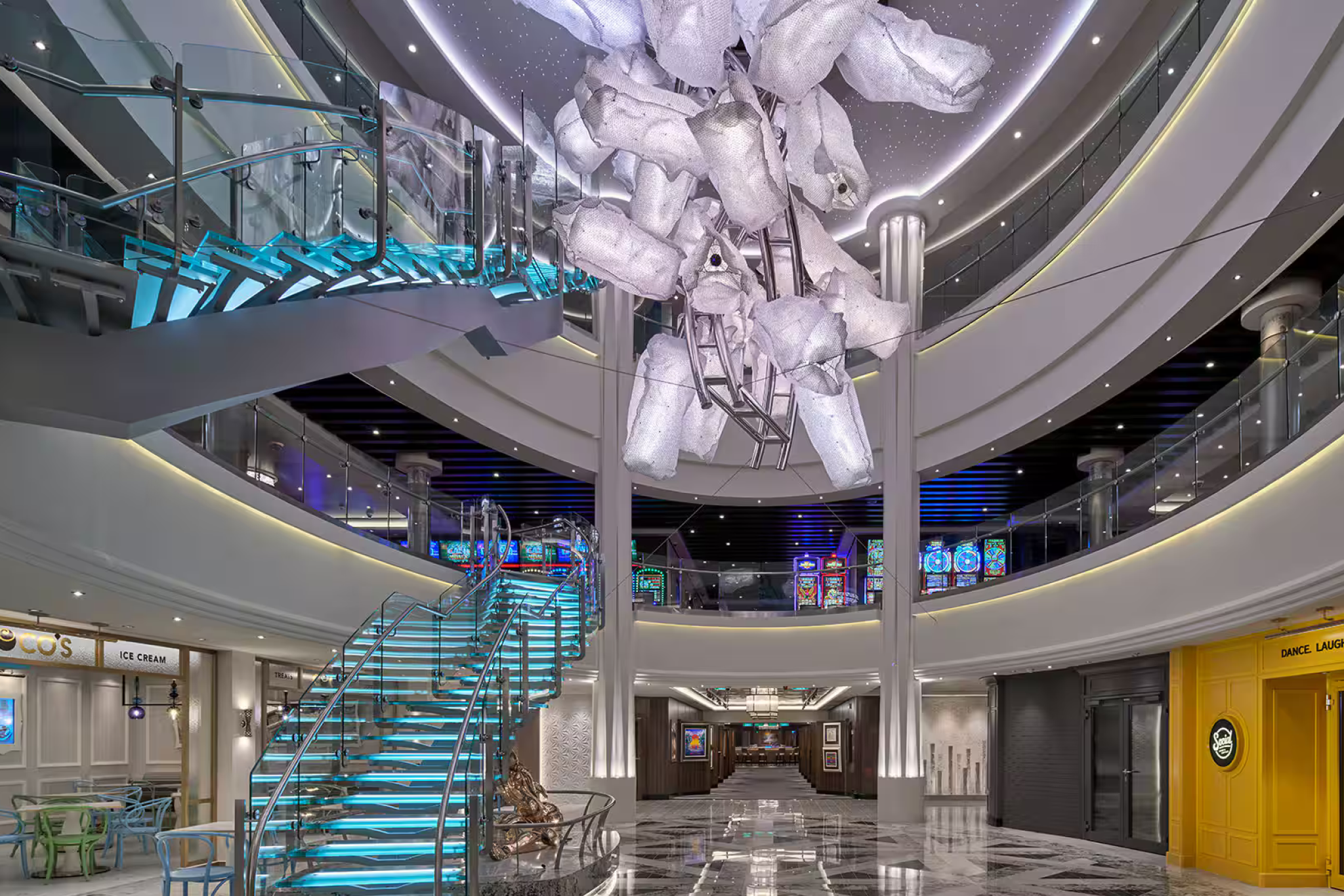 Modern atrium inside Norwegian Encore with LED-lit staircase, artistic chandelier, and stylish public space design.