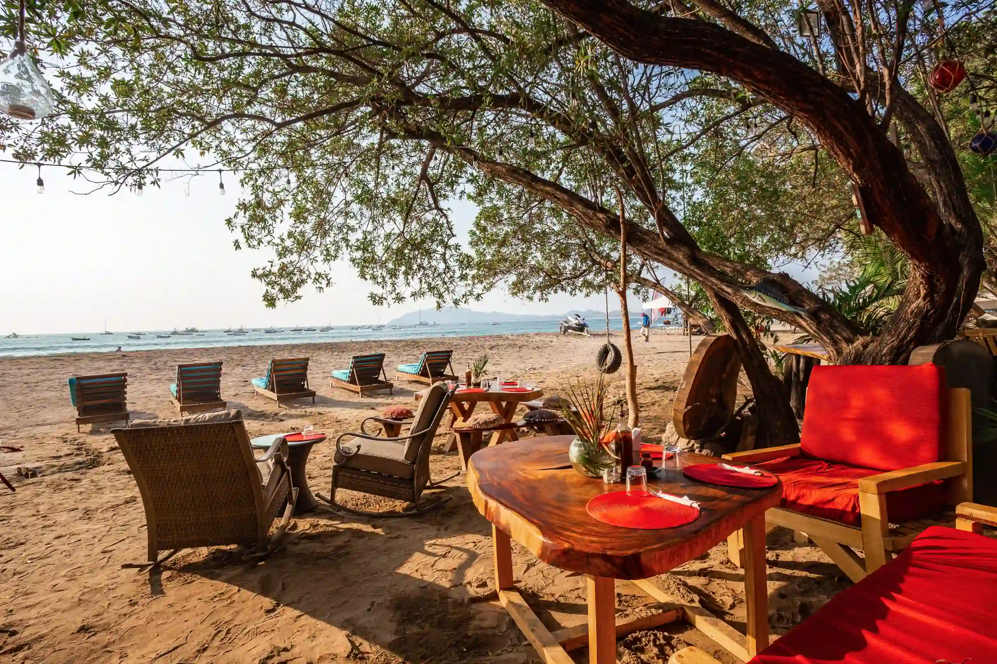 View of the beachfront from Ocho Artisan Bungalows, showing calm waves, golden sand, and blue umbrellas.