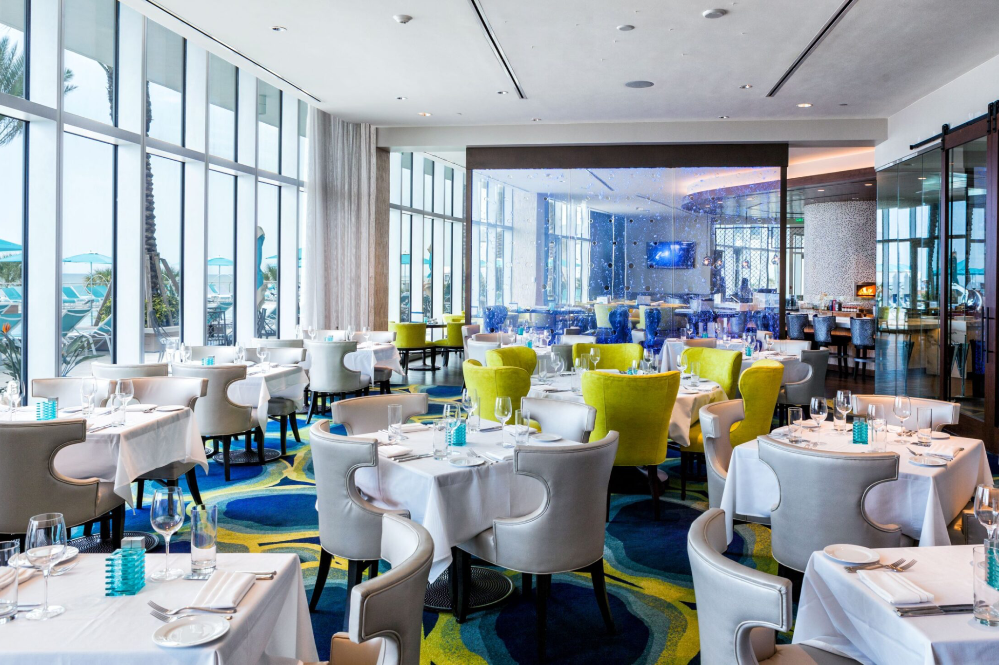 Bright, modern dining space at Opal Sands Resort’s Sea-Guini restaurant, featuring floor-to-ceiling windows with ocean views and contemporary seating.
