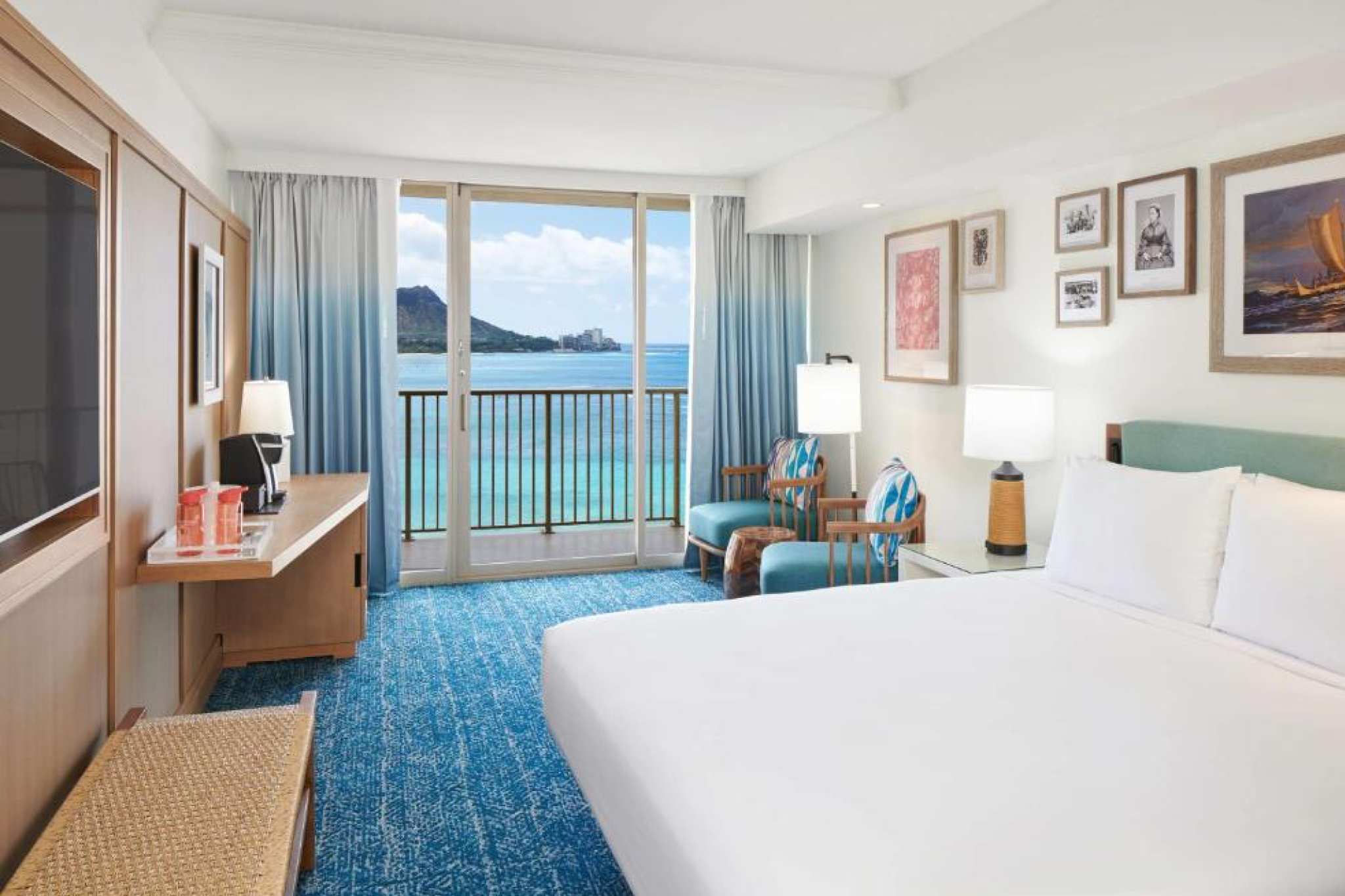Interior of an oceanfront guest room at Outrigger Reef Waikiki Beach Resort, featuring a king bed, seating area, and balcony with views of Diamond Head and the Pacific Ocean.