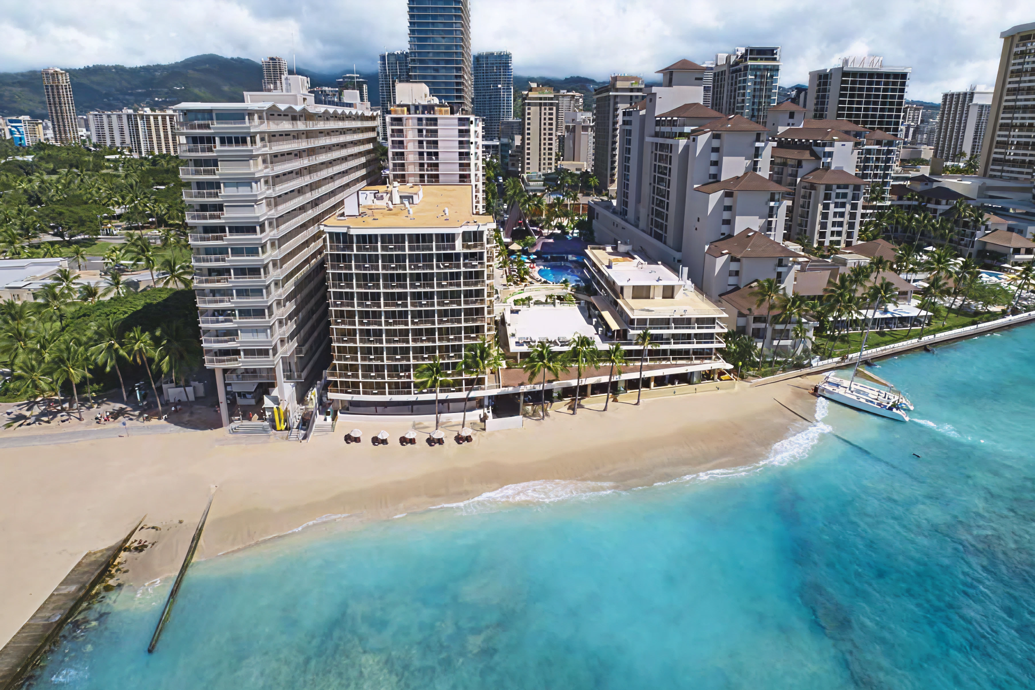 Aerial view of the beachfront location of Outrigger Reef Waikiki Beach Resort, showing direct beach access and surrounding high-rise buildings in Waikīkī, Honolulu.