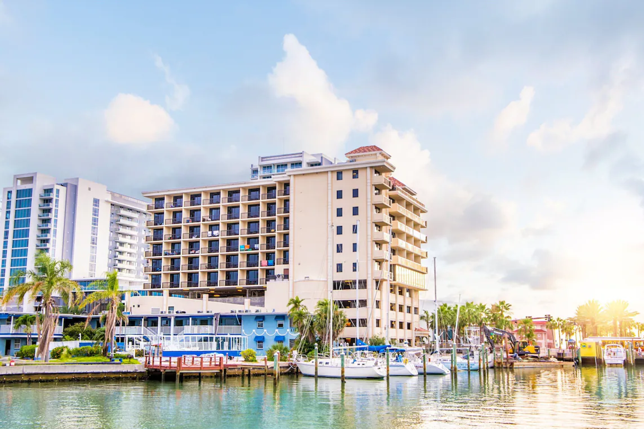 Exterior view of Pier House 60 Clearwater Beach Marina Hotel from the marina, with sailboats docked and palm trees lining the waterfront.