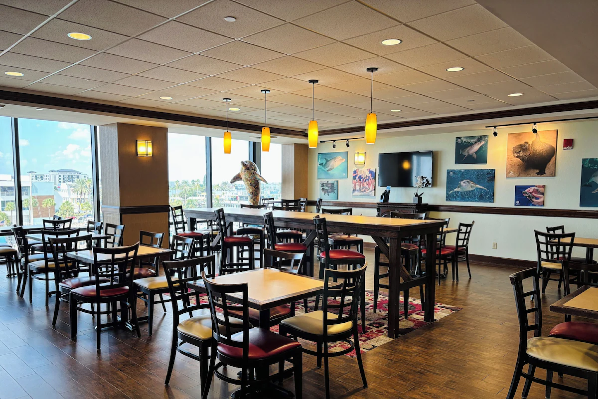 Bright breakfast area inside Pier House 60 Clearwater Beach Marina Hotel, featuring dining tables, ocean-themed wall art, and large windows with city views.