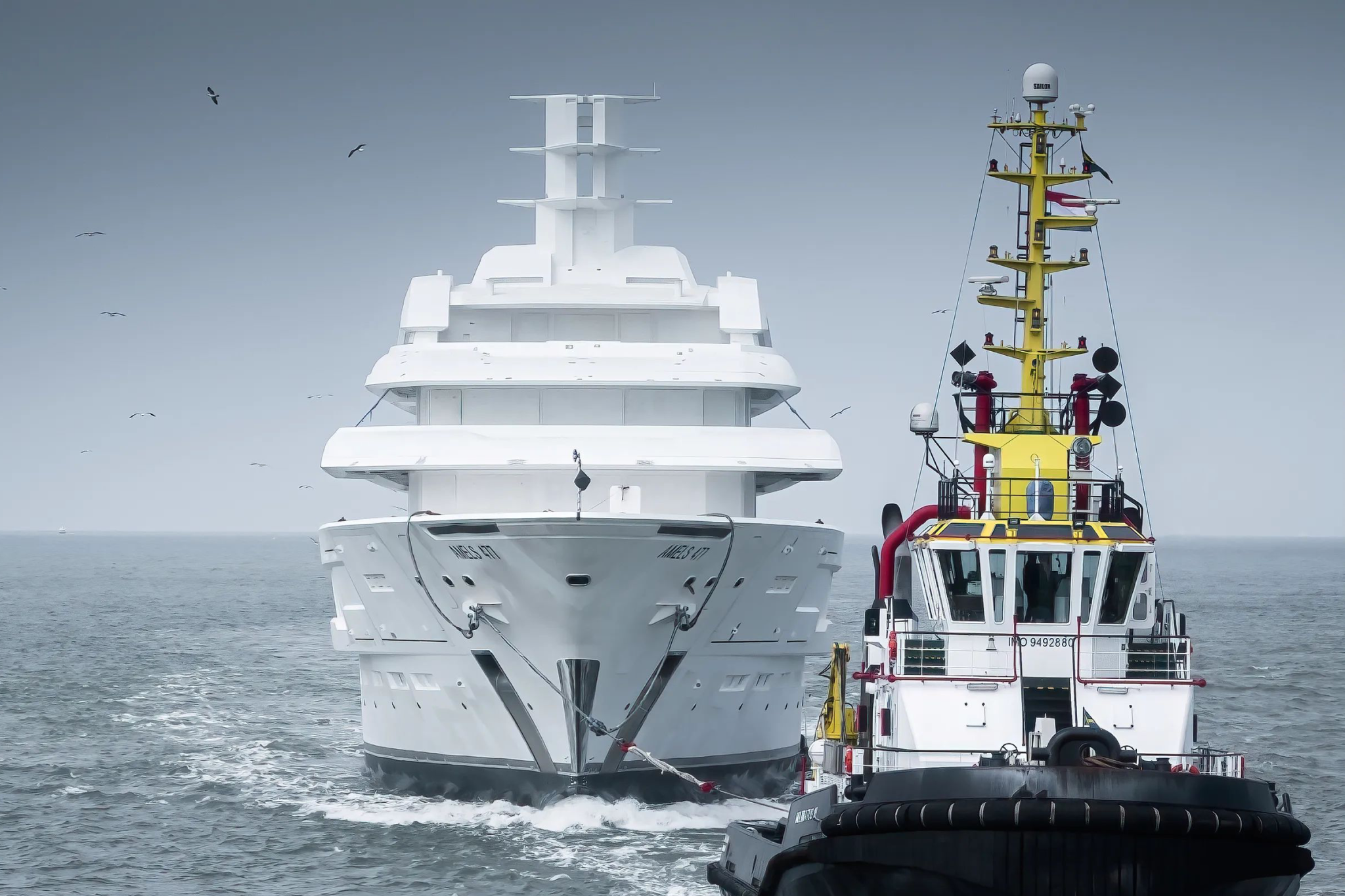 Bow-on view of Project Tanzanite during harbor maneuvers alongside a tugboat, emphasizing the yacht’s commanding presence, vertical bow, and readiness for final sea trials ahead of its 2026 delivery.
