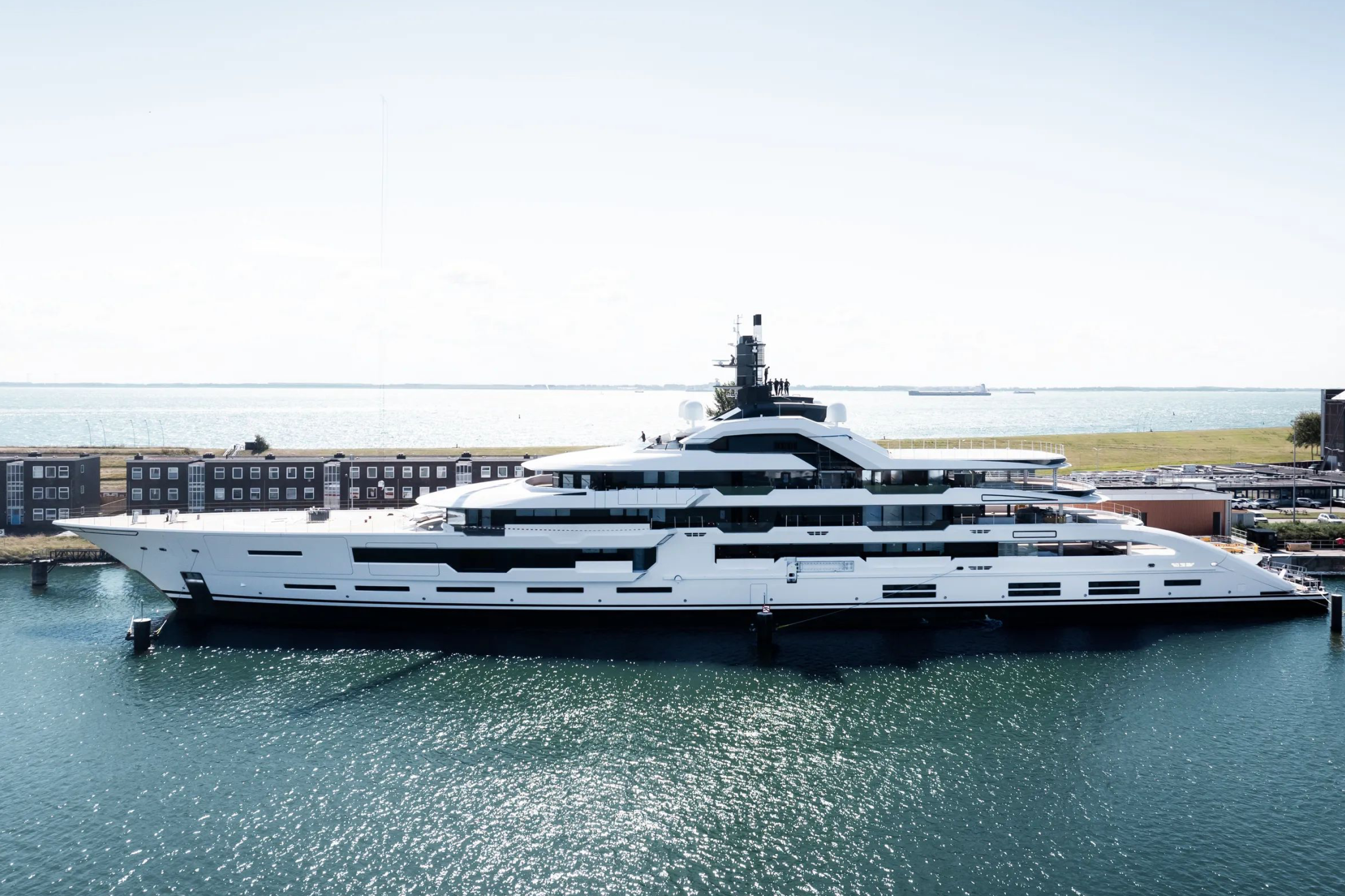 Project Tanzanite superyacht moored during outfitting, shown in full side profile with its 120-meter white hull, five-deck layout, and Espen Øino exterior design at the Amels shipyard.