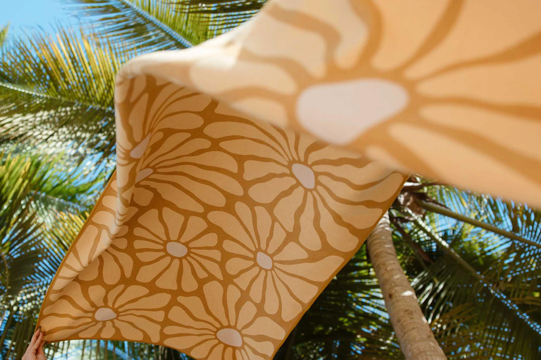 Golden Nomadix Original towel with floral pattern fluttering under palm trees, showcasing versatility and performance as one of the Best Quick-Dry Towels for the Beach.