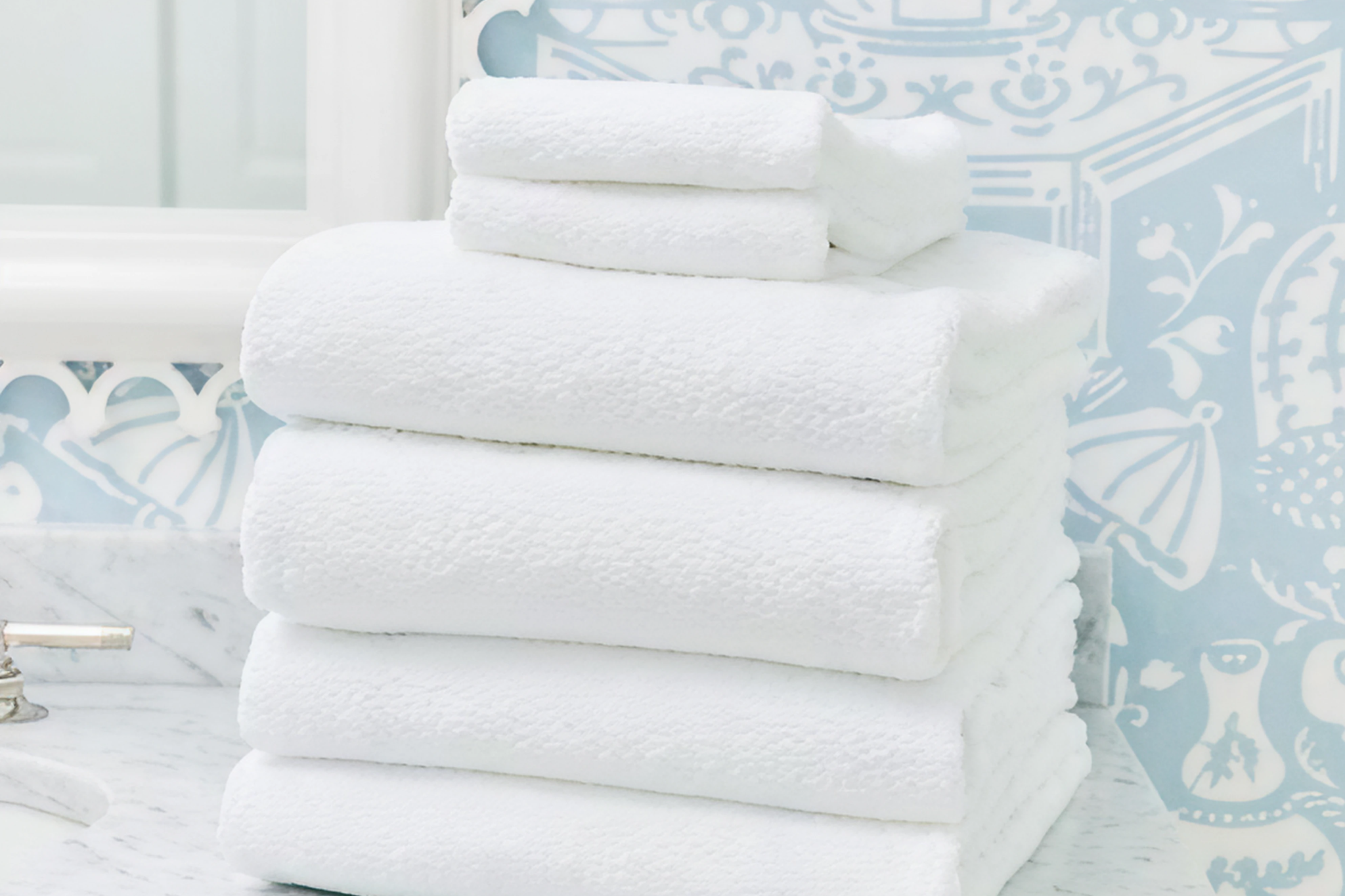Stack of white Weezie Beach Towels arranged in a bright bathroom, illustrating plush softness and quick-drying capability among the Best Quick-Dry Towels for the Beach.
