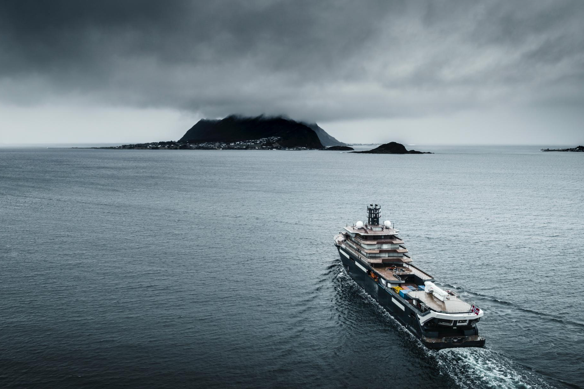 Aerial view of REV Ocean navigating open waters beneath dramatic overcast skies, emphasizing its massive footprint, polar-capable hull, and role as the world’s largest mission-driven research superyacht.