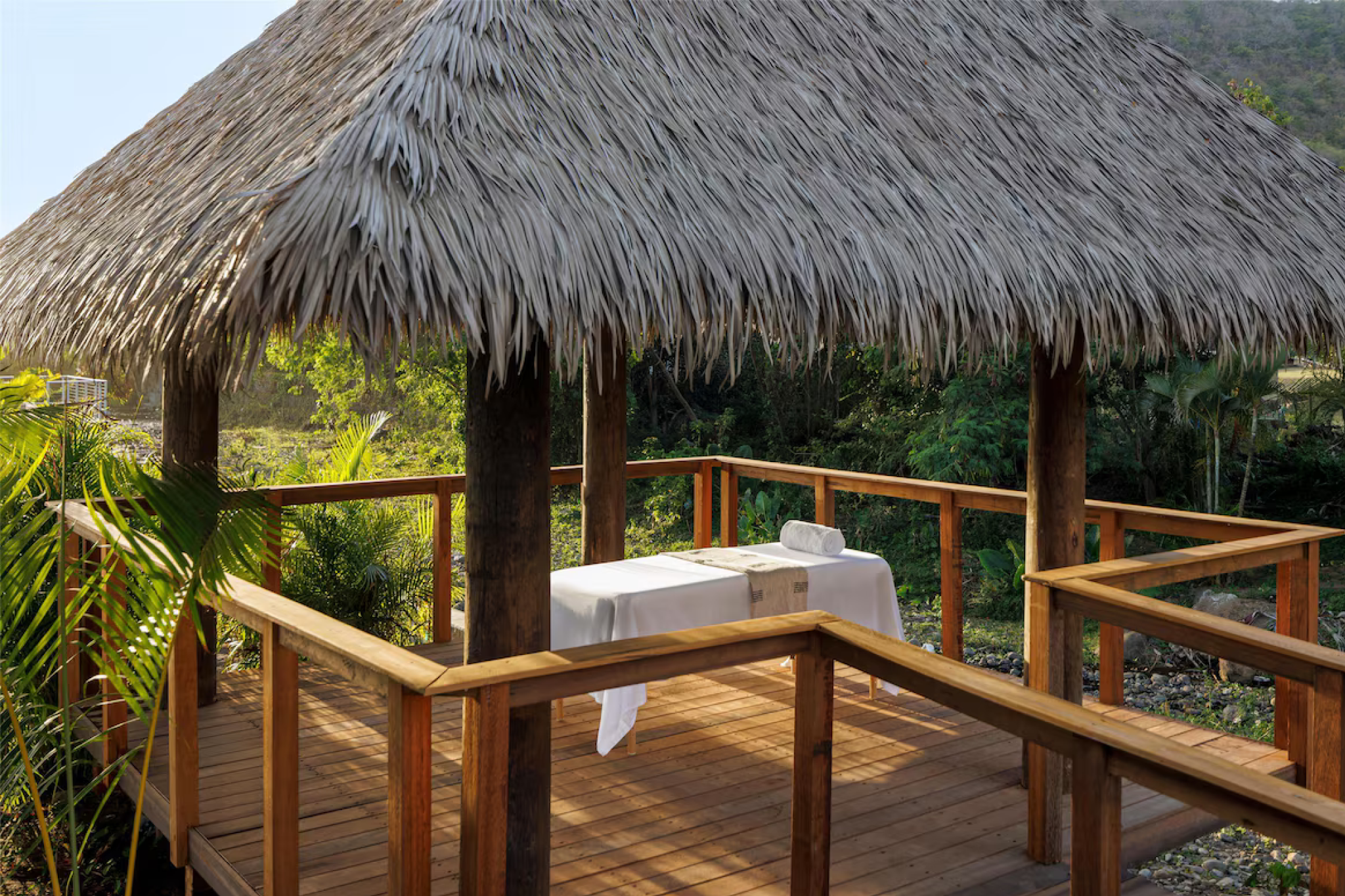 Thatched-roof open-air spa pavilion at Sandals Saint Vincent, nestled in lush tropical greenery and surrounded by forest views for a serene massage experience.