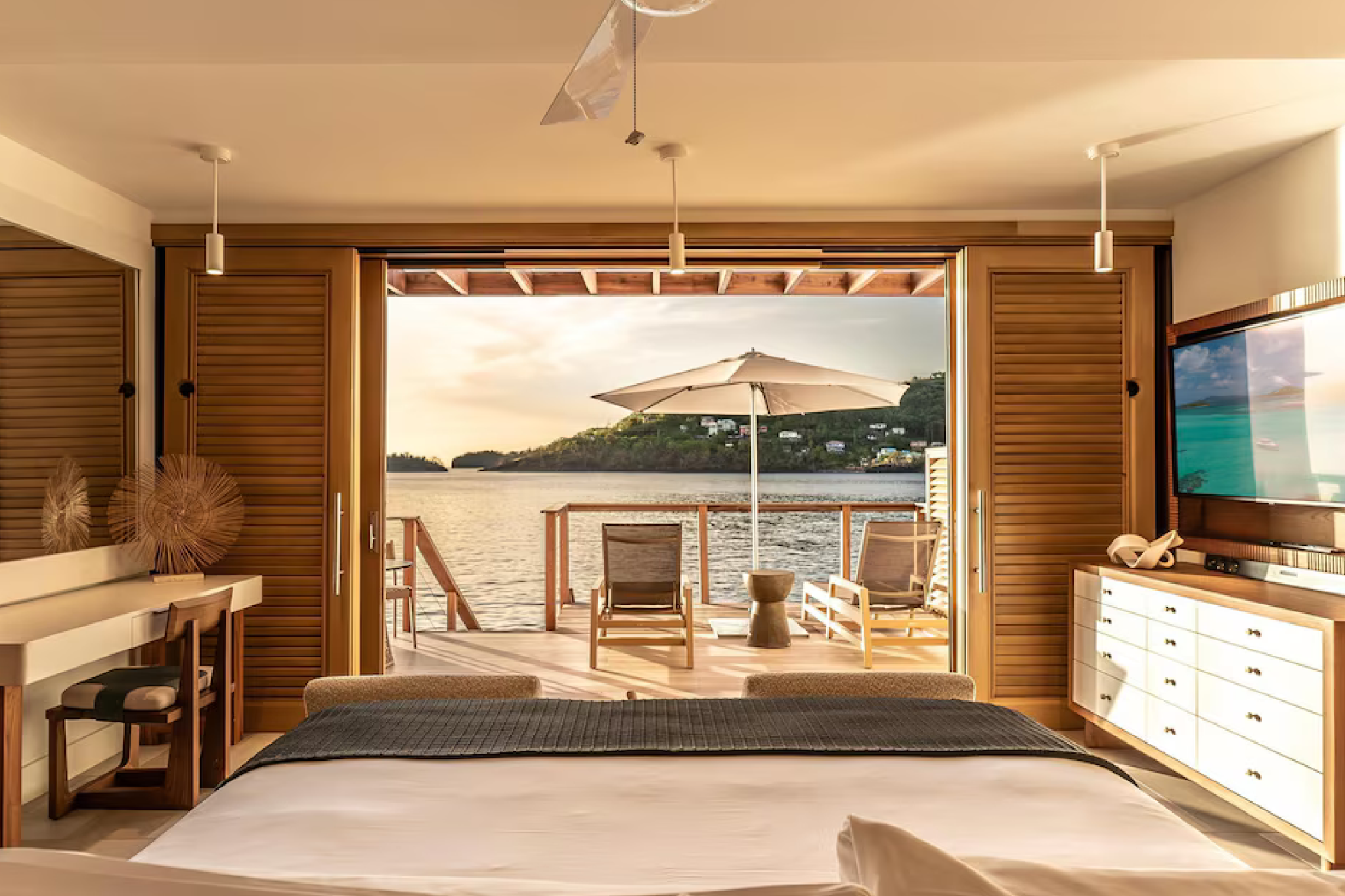 Luxury overwater villa suite at Sandals Saint Vincent with an ocean-facing bed, private deck, lounge chairs, and panoramic views of the Caribbean Sea.