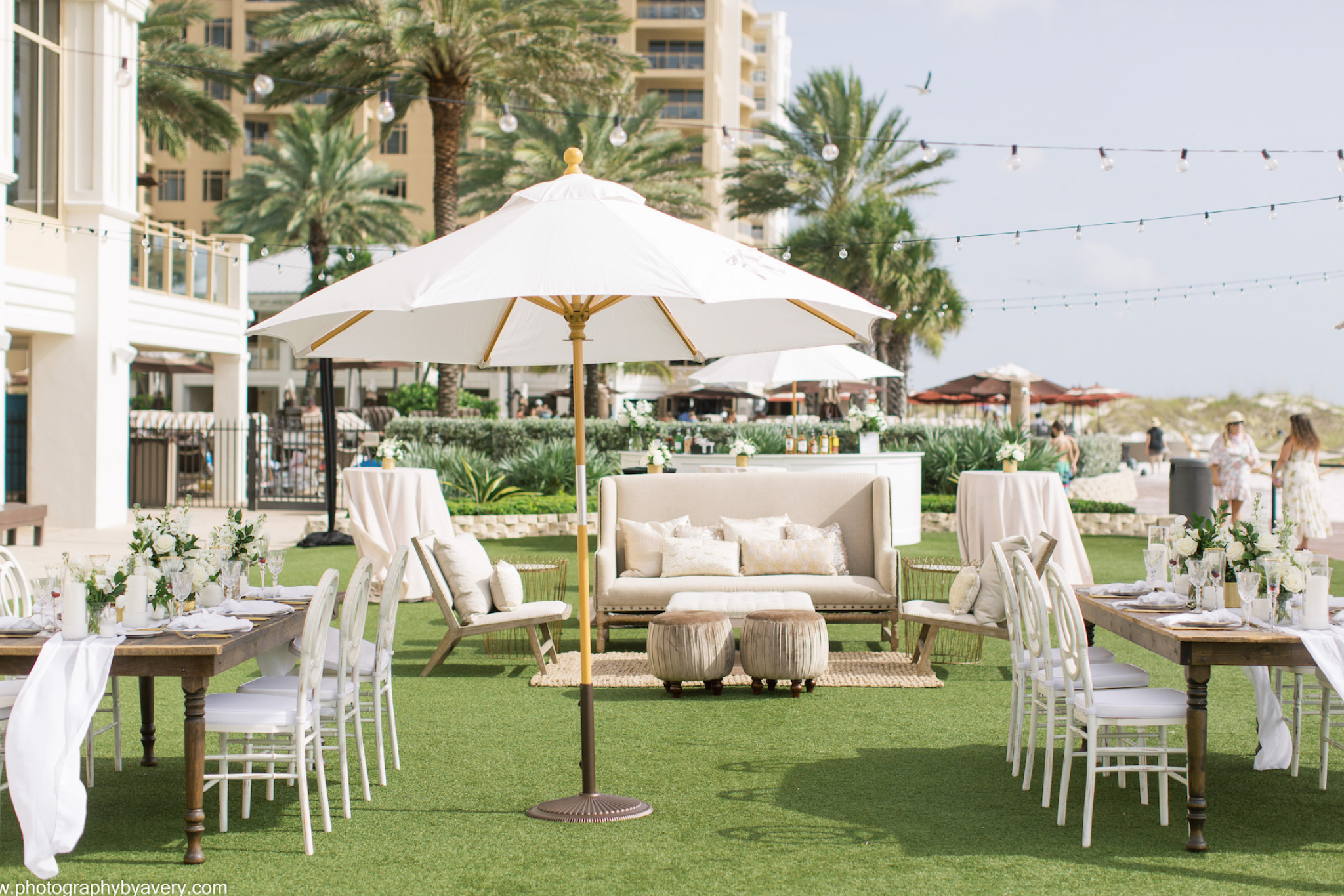 Elegant outdoor event setup at Sandpearl Resort featuring white umbrellas, floral centerpieces, and stylish seating under string lights near the beach.