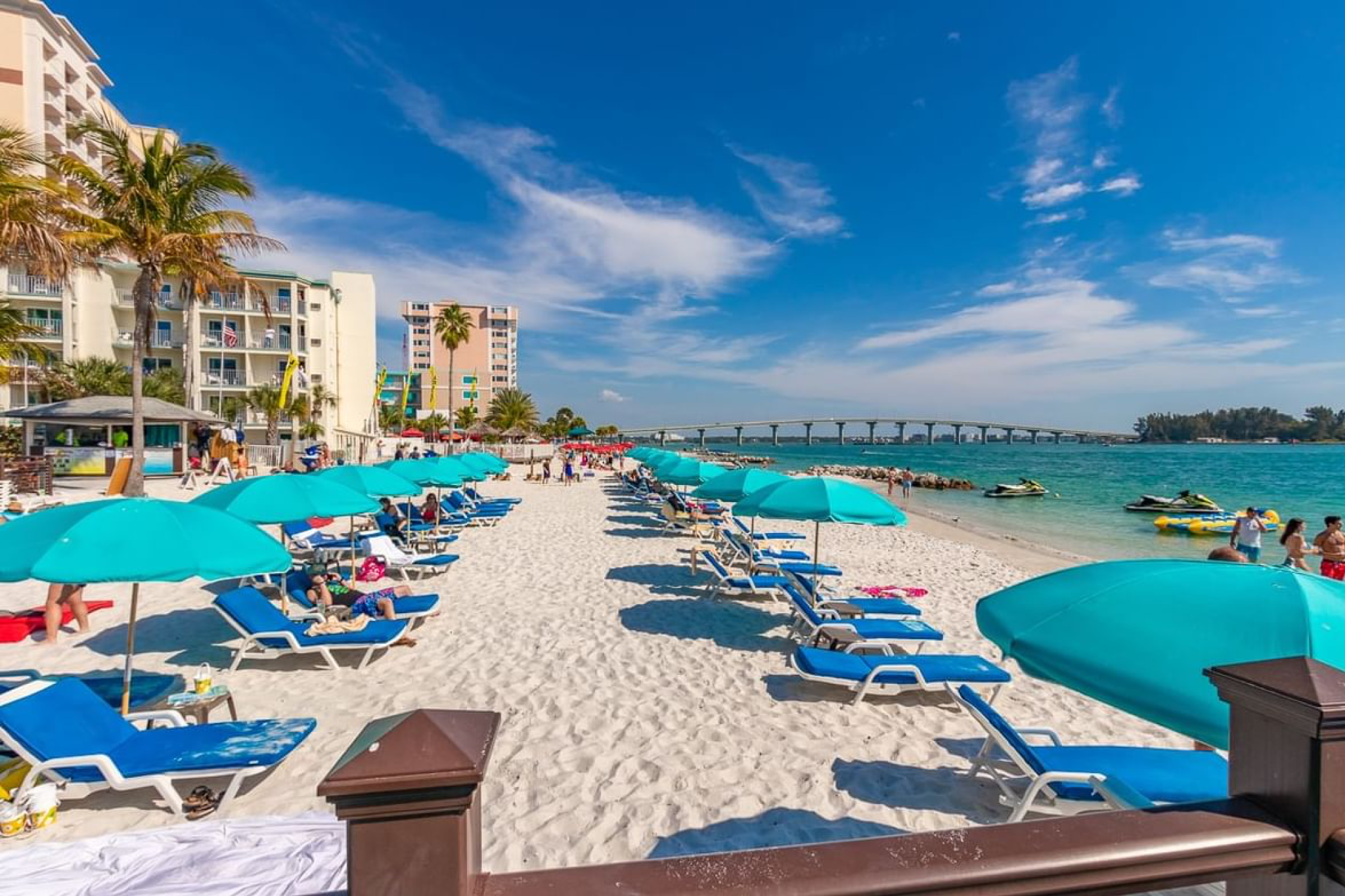 White sand beachfront lined with teal umbrellas and lounge chairs directly in front of Shephard’s Beach Resort Clearwater.