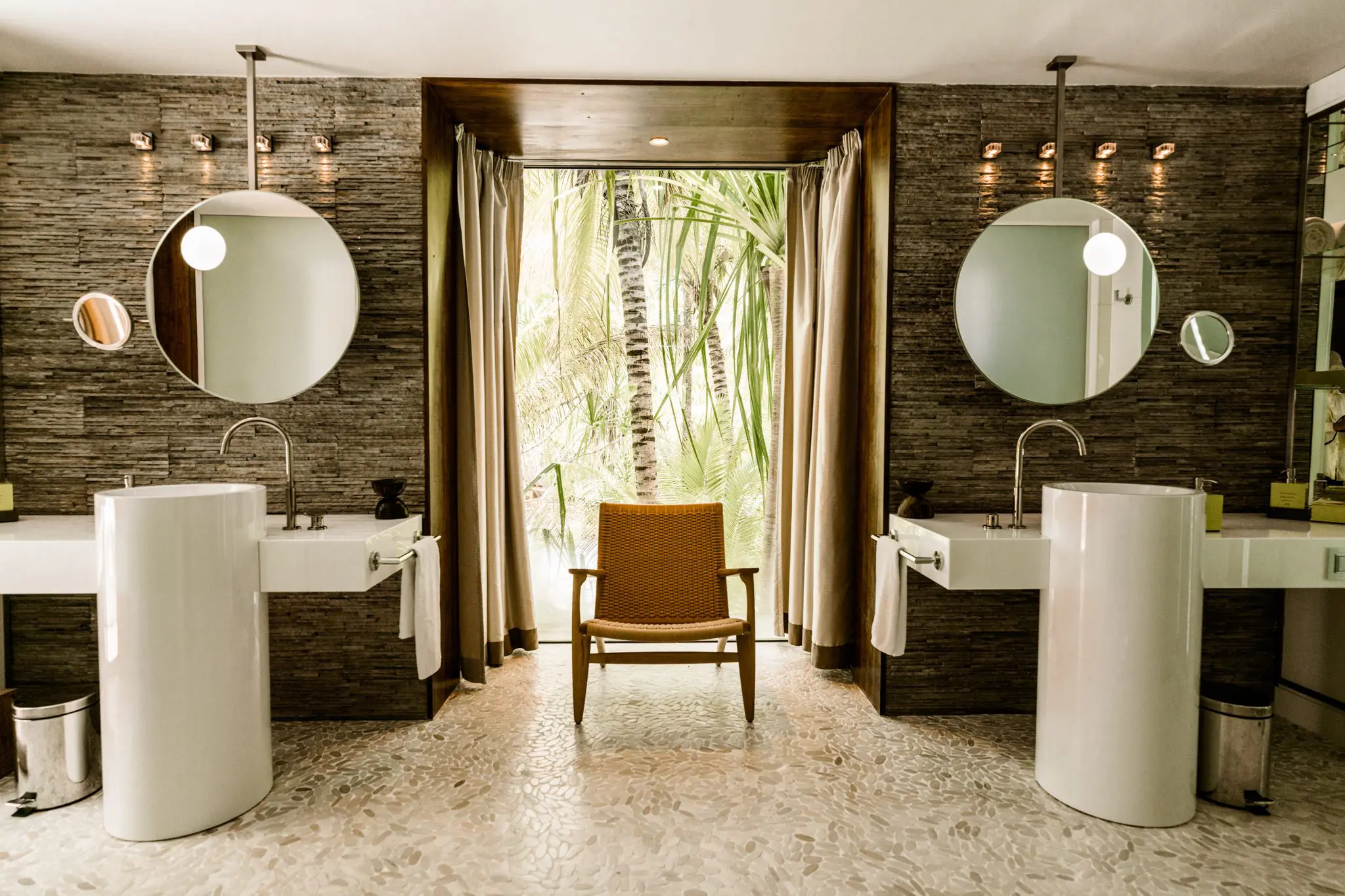 Elegant spa-style bathroom at The Brando with dual vanities, round mirrors, and a tropical garden view—highlighting design without excess.