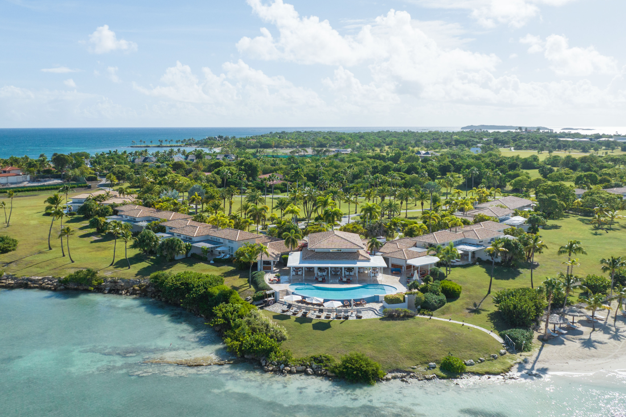 A private-island coastline with Jumby Bay’s elegant villas and a central infinity-edge pool surrounded by lush greenery, opening onto tranquil Caribbean waters — showcasing why it remains one of the top resorts in the Caribbean Islands in 2025.