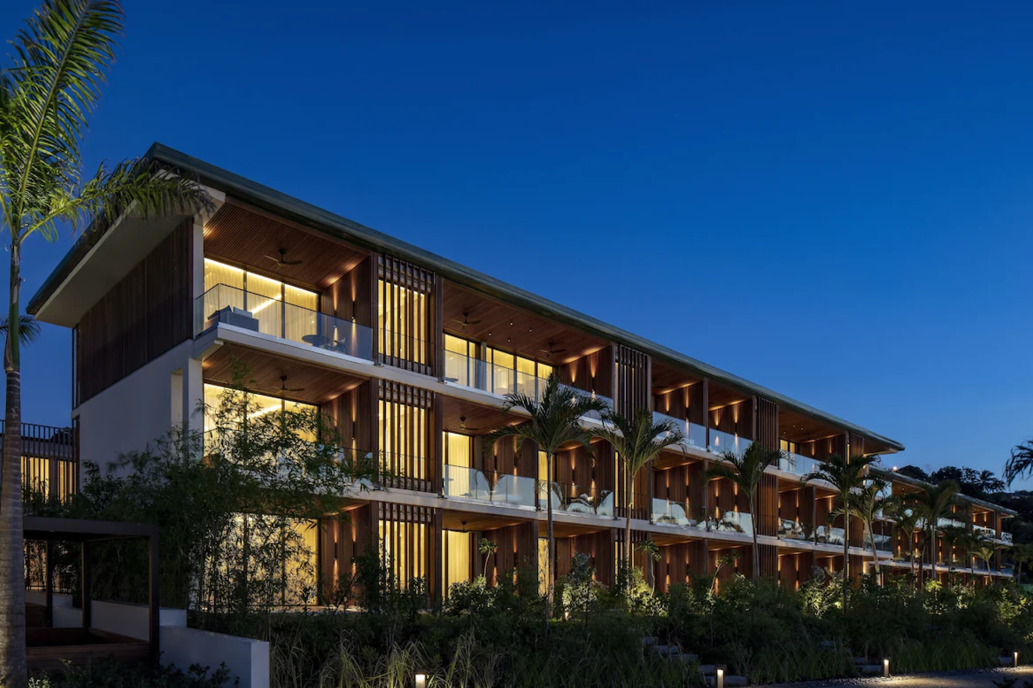 A modern, minimalist beachfront building at Silversands Grenada glowing warmly at dusk, with clean architectural lines, tall palms, and open balconies — a striking example of contemporary luxury among the top resorts in the Caribbean Islands in 2025.
