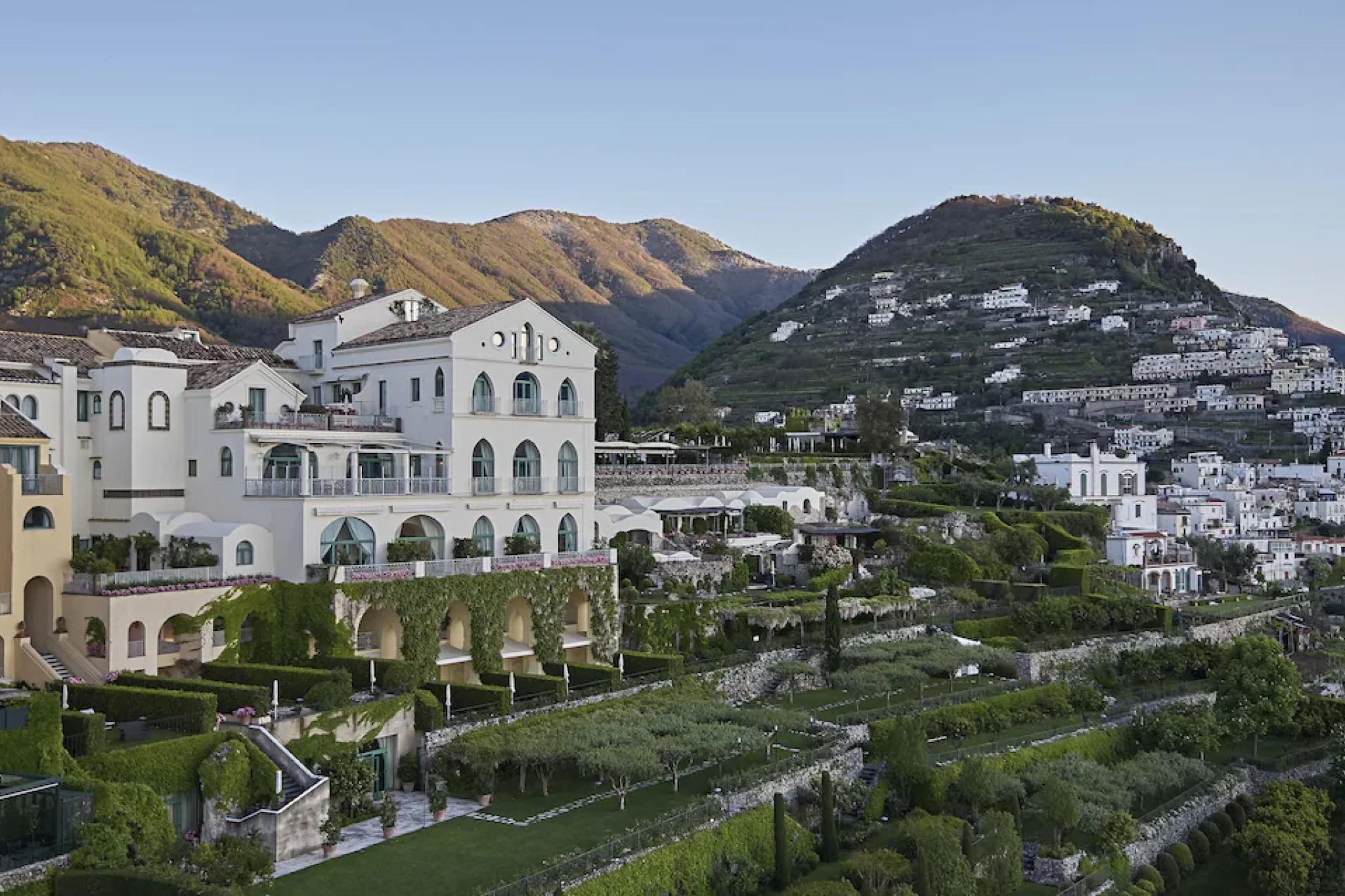A majestic view of Belmond Hotel Caruso perched high above Ravello, surrounded by terraced Italian gardens and mountain scenery overlooking the Amalfi Coast — a timeless, romantic icon among the top resorts in the Mediterranean in 2025.