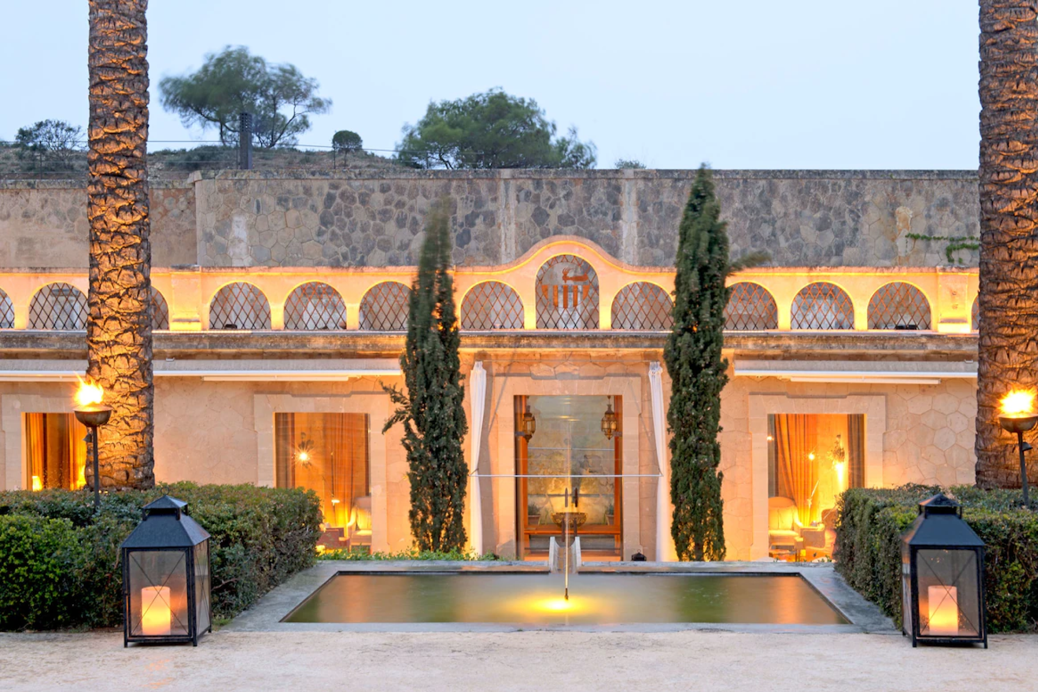 The historic stone façade of Cap Rocat at dusk, with fortress walls, lantern-lit pathways, and serene courtyard landscaping — a uniquely atmospheric heritage retreat recognized as one of the top resorts in the Mediterranean in 2025.