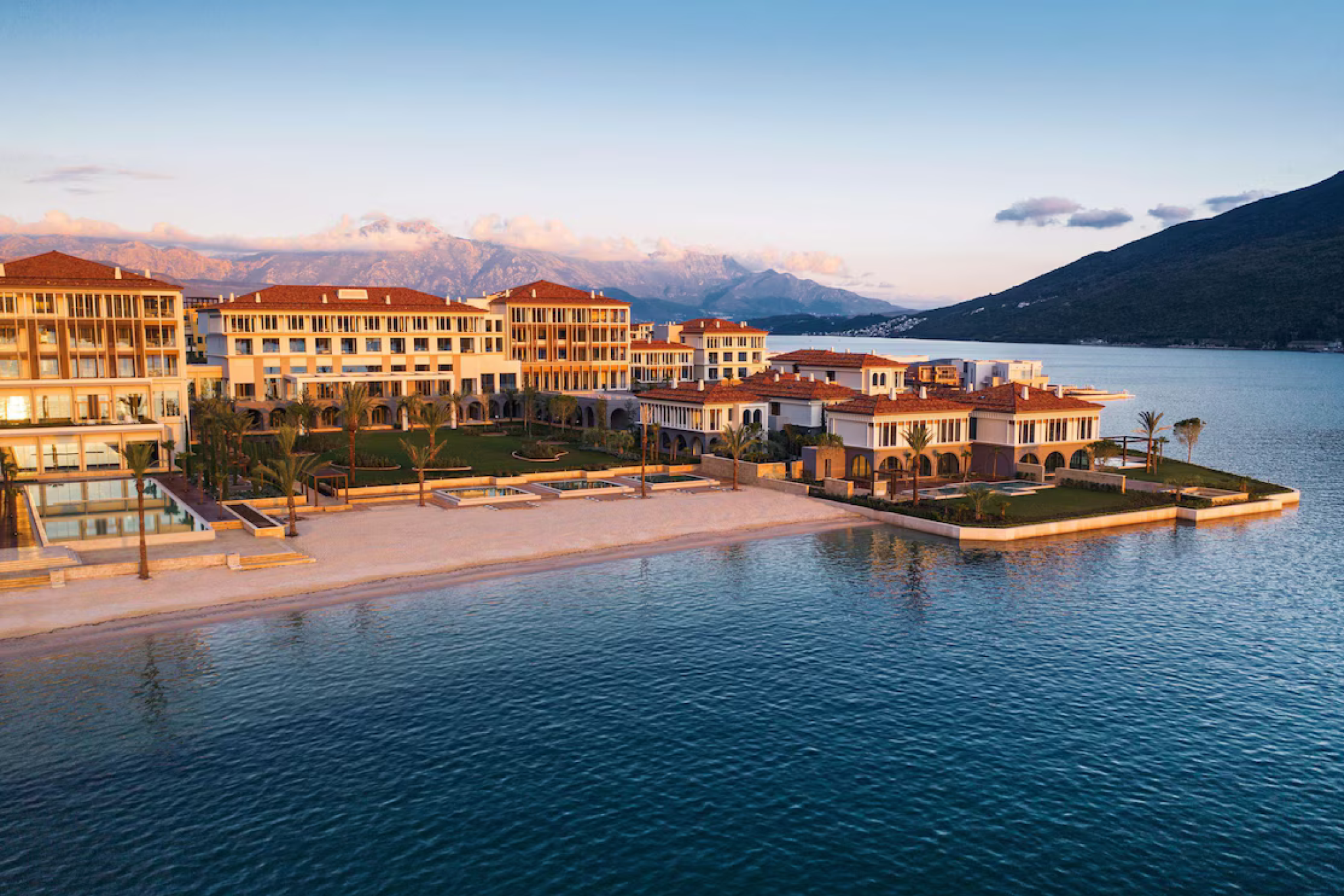 A golden-hour aerial view of One&Only Portonovi, showcasing its grand waterfront palatial buildings, manicured gardens, and marina-side setting along Montenegro’s Bay of Kotor — a standout among the top resorts in the Mediterranean in 2025.