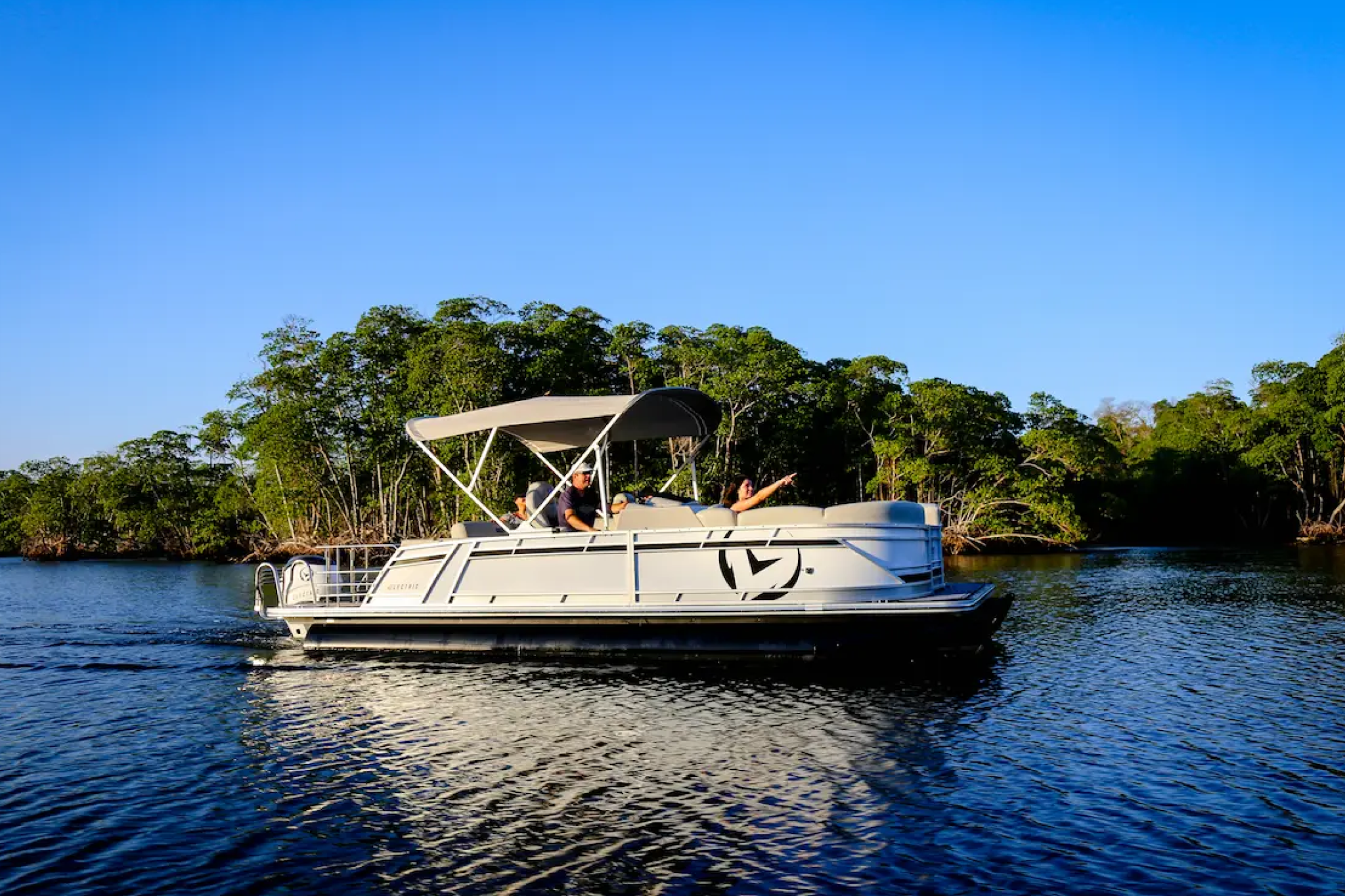 The V24 Electric Pontoon cruising on calm water, showing its spacious seating layout, aluminum pontoons, and electric outboard configuration as part of its key specifications.